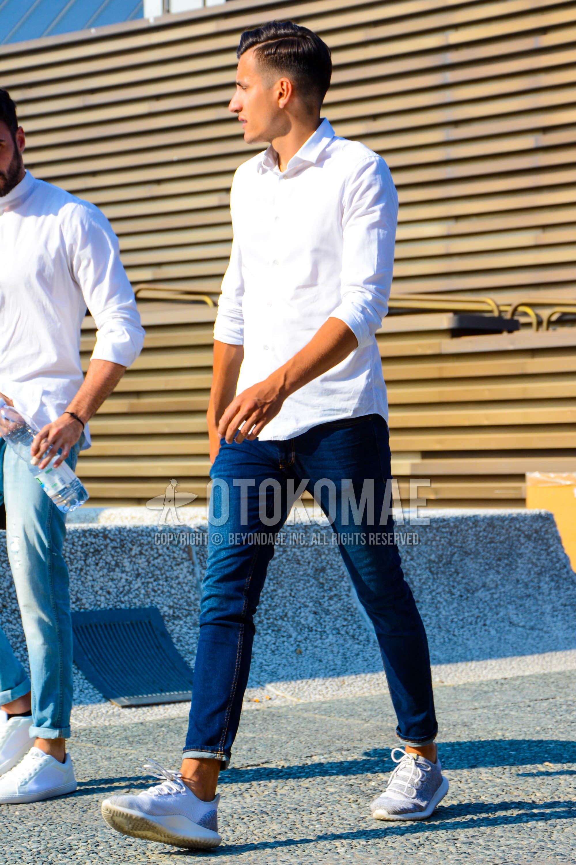 Men's spring summer outfit with white plain shirt, blue plain denim/jeans, white low-cut sneakers.