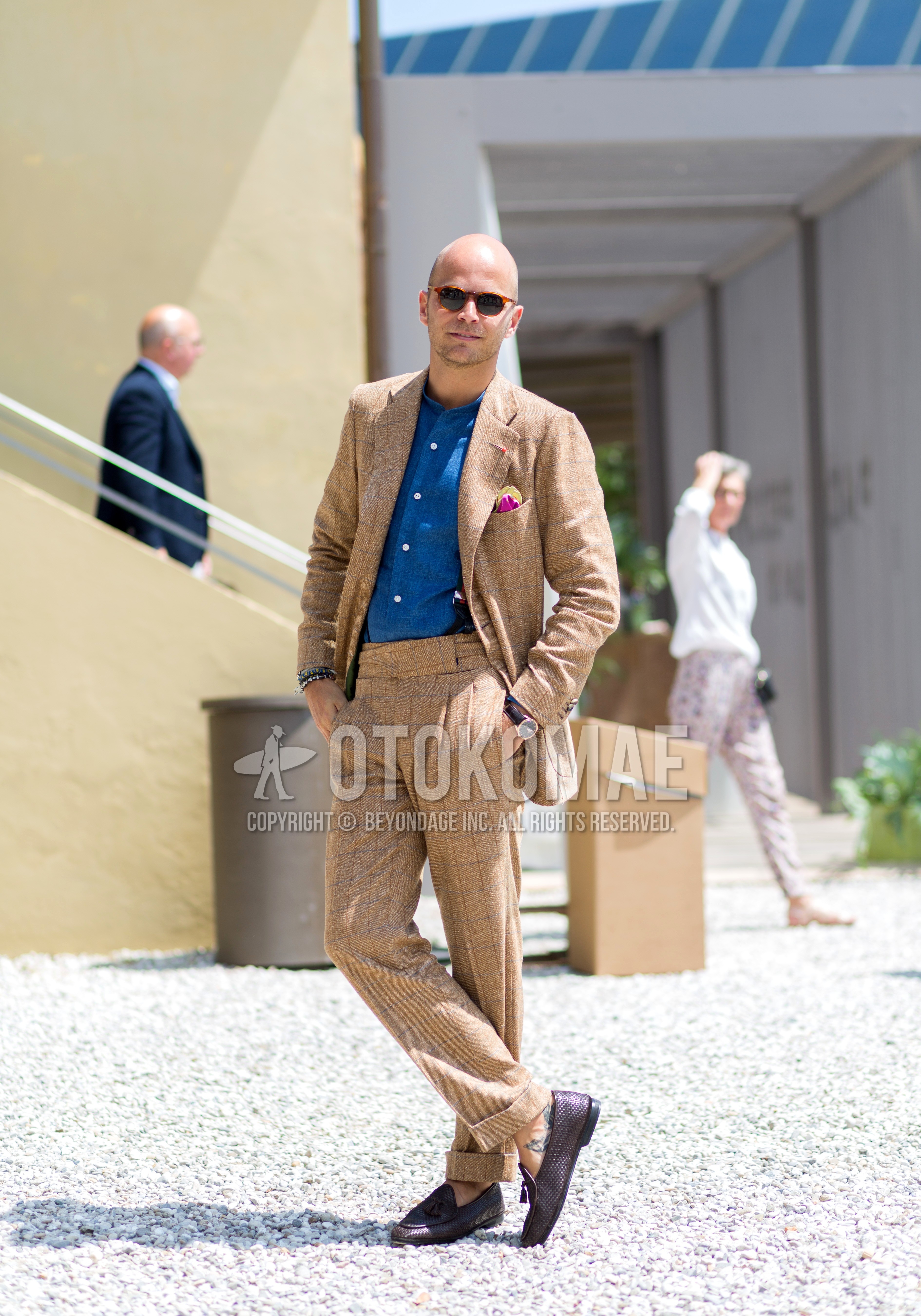 Men's spring winter outfit with brown tortoiseshell sunglasses, blue plain shirt, brown purple tassel loafers leather shoes, beige brown check suit.