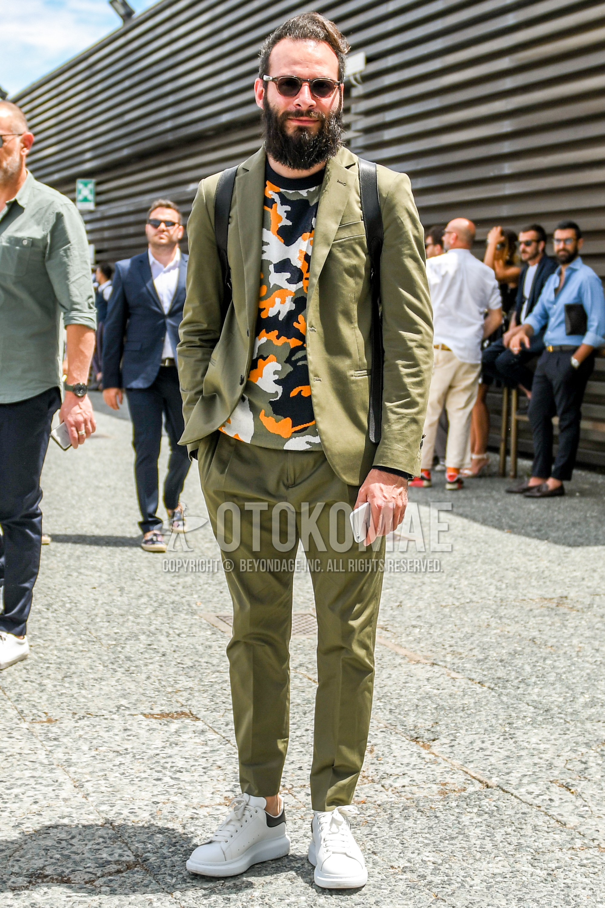 Men's spring summer autumn outfit with plain sunglasses, multi-color camouflage t-shirt, white low-cut sneakers, olive green plain suit.