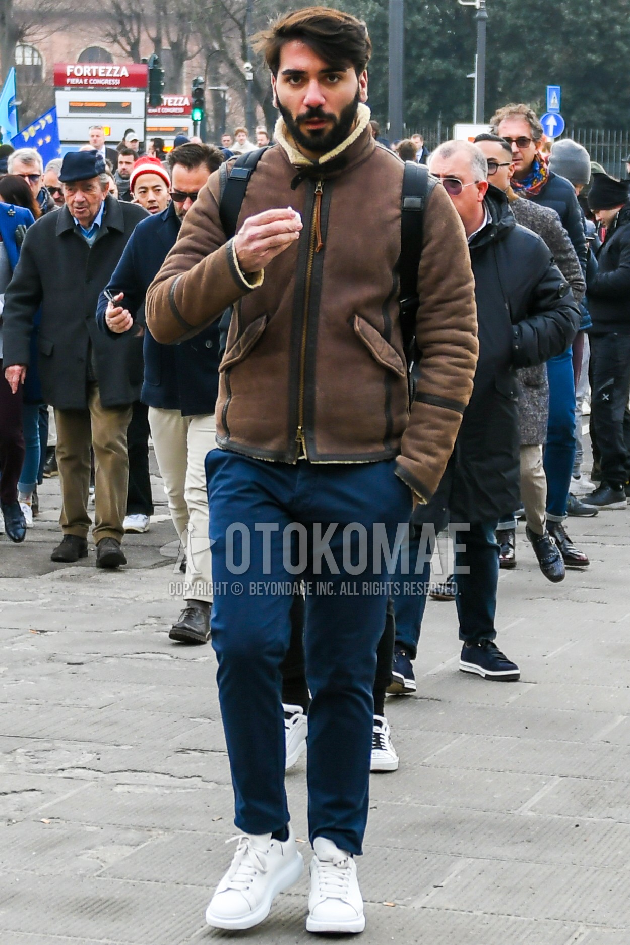 Men's autumn winter outfit with brown plain leather jacket, navy plain chinos, white low-cut sneakers.