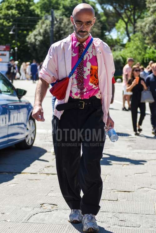 ブラウン無地のメガネ、ピンク無地のマウンテンパーカー、ピンクボタニカルのシャツ、黒無地のレザーベルト、ダークグレー無地のスラックス、グレーローカットのスニーカー、レッド無地のサコッシュ、レッドネクタイのネクタイを合わせた春秋のメンズコーデ・着こなし。