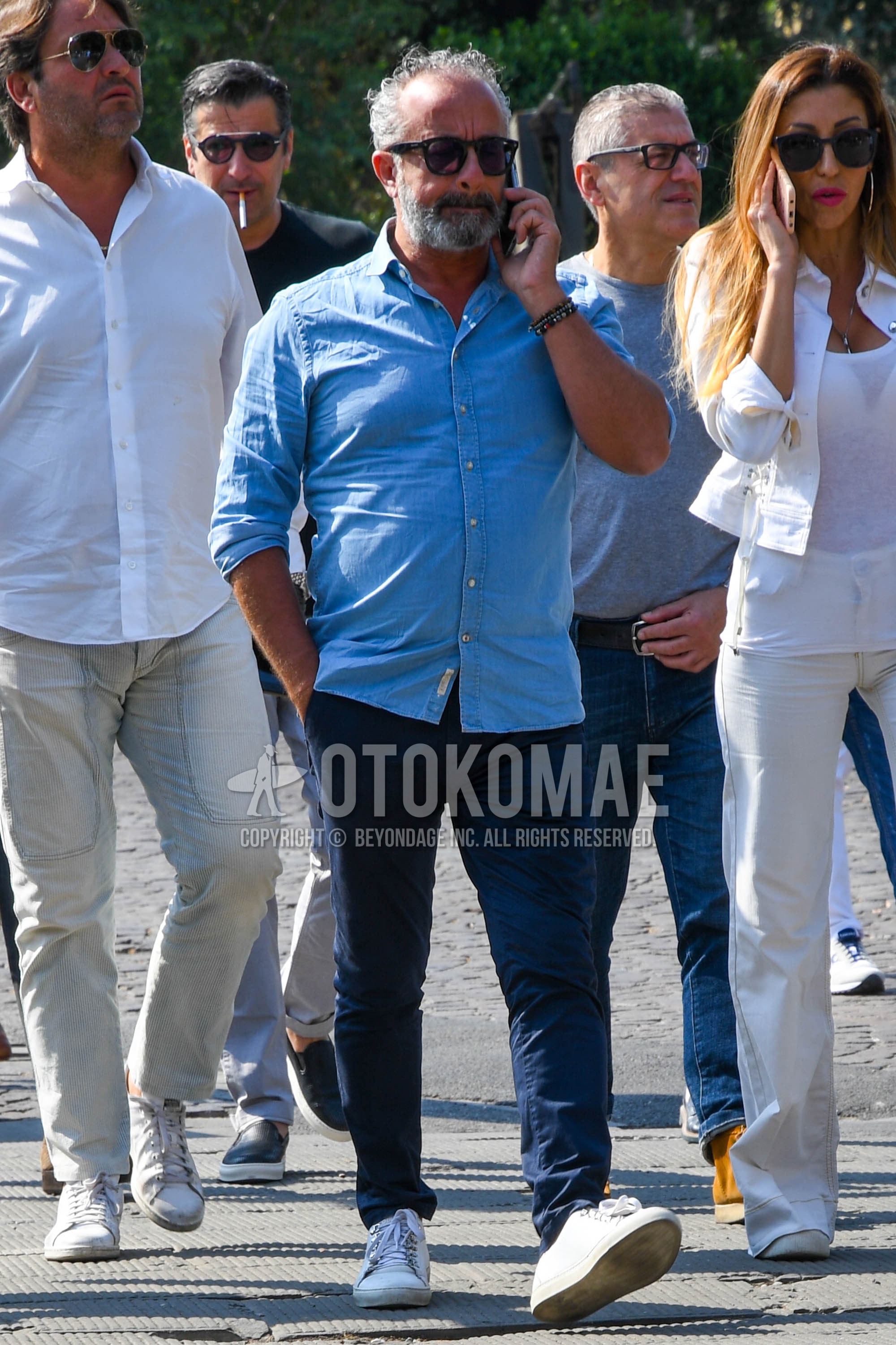 Men's spring summer outfit with plain sunglasses, light blue plain denim shirt/chambray shirt, navy plain chinos, white low-cut sneakers.