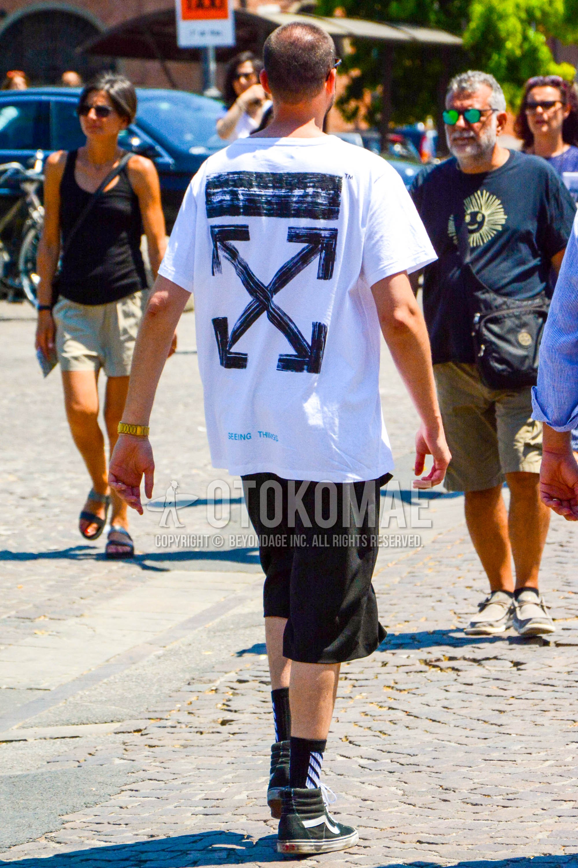 Men's summer outfit with white graphic t-shirt, black plain short pants, black graphic socks, black high-cut sneakers.