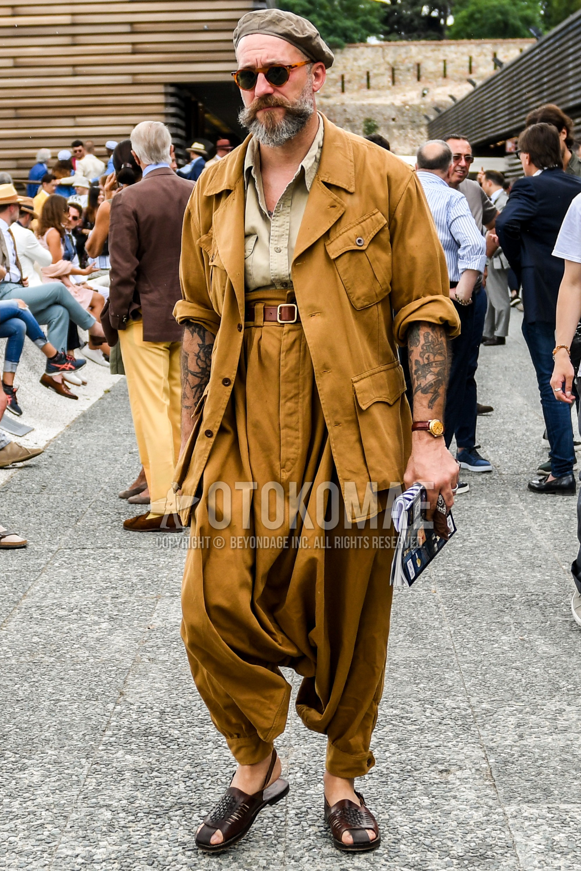 Men's spring summer autumn outfit with tortoiseshell sunglasses, beige plain safari jacket, beige plain shirt, brown plain leather belt, beige plain suluell pants, brown leather sandals.