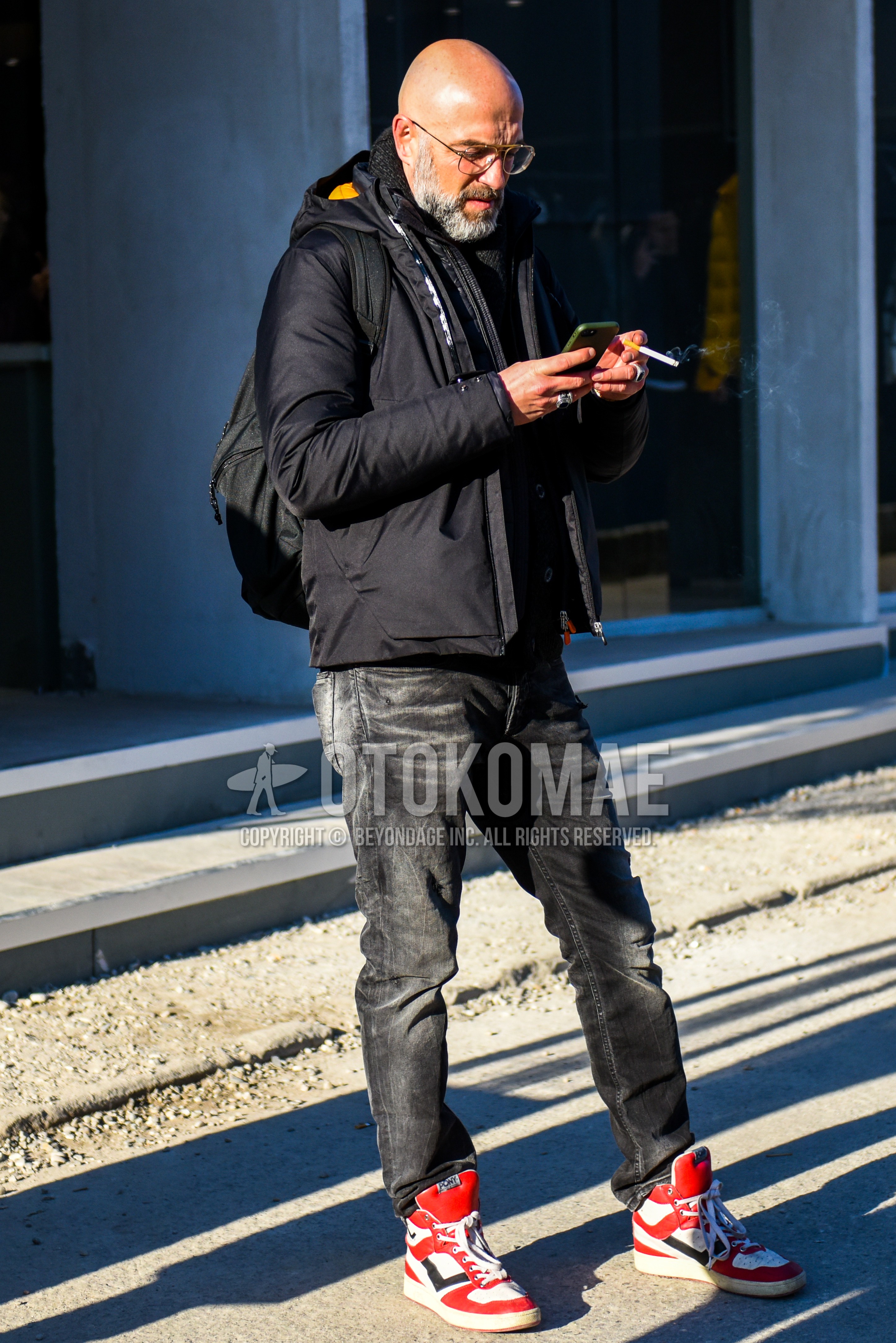 Men's winter outfit with plain glasses, black plain down jacket, dark gray plain denim/jeans, red high-cut sneakers.
