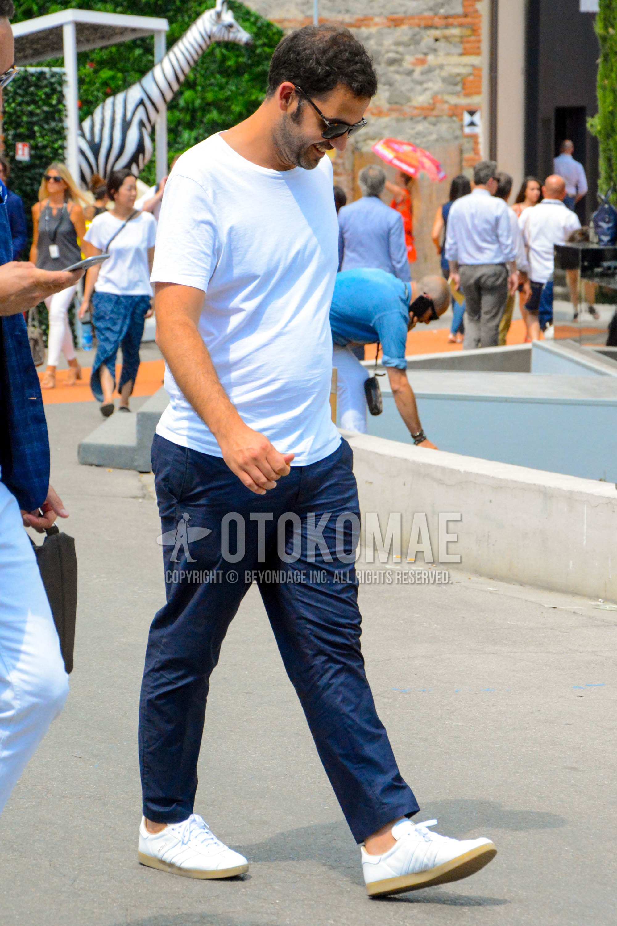 Men's summer outfit with plain sunglasses, white plain t-shirt, blue plain ankle pants, blue plain chinos, white low-cut sneakers.