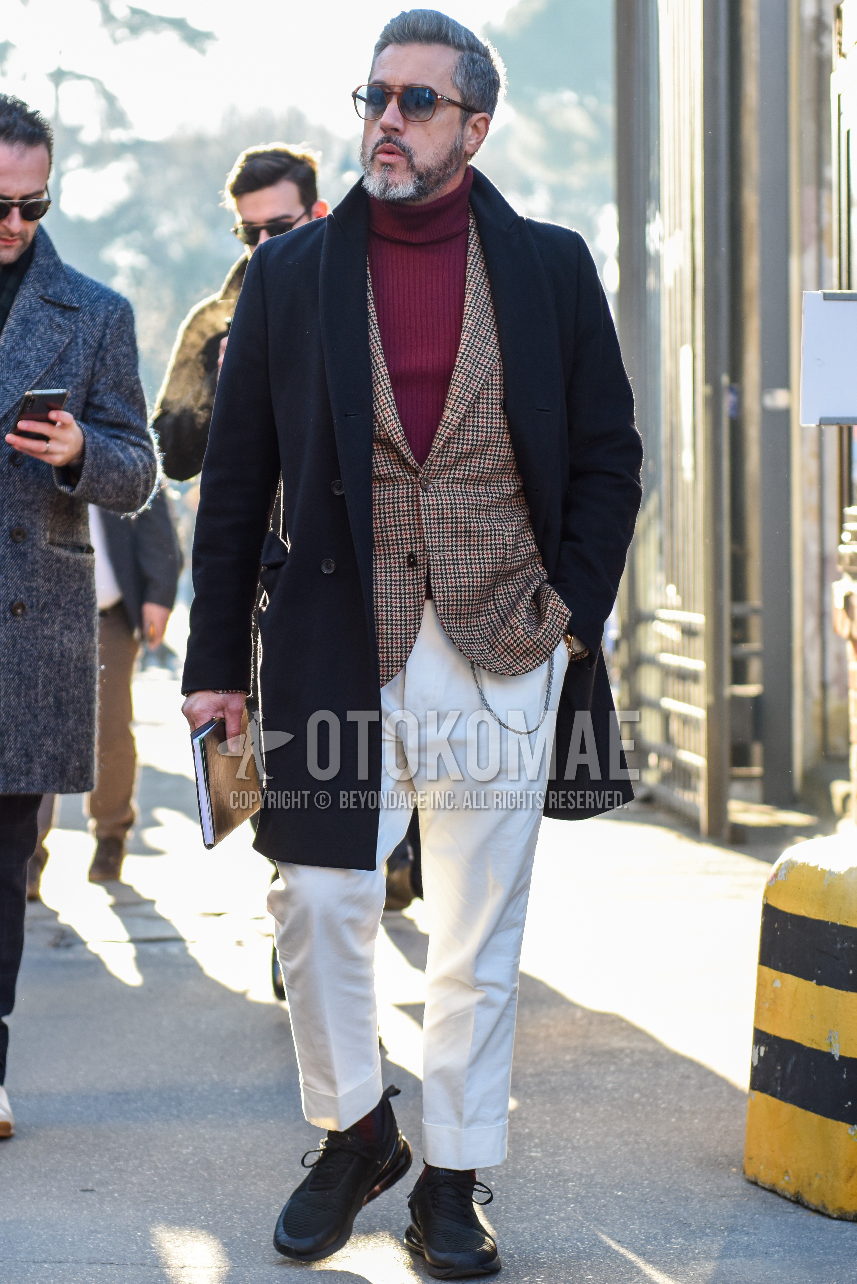 Men's autumn winter outfit with brown tortoiseshell sunglasses, dark gray plain chester coat, beige check tailored jacket, red plain turtleneck knit, white plain cotton pants, red plain socks, black low-cut sneakers.