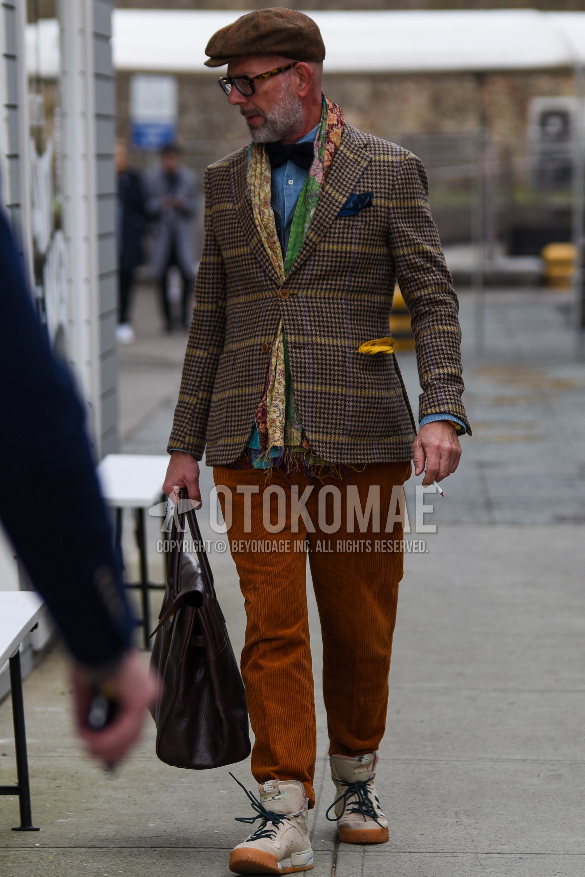 Men's autumn winter outfit with brown plain hunting cap, brown tortoiseshell glasses, multi-color scarf scarf, brown check tailored jacket, blue plain denim shirt/chambray shirt, brown plain winter pants (corduroy,velour), beige high-cut sneakers, brown plain briefcase/handbag, black plain bow tie.