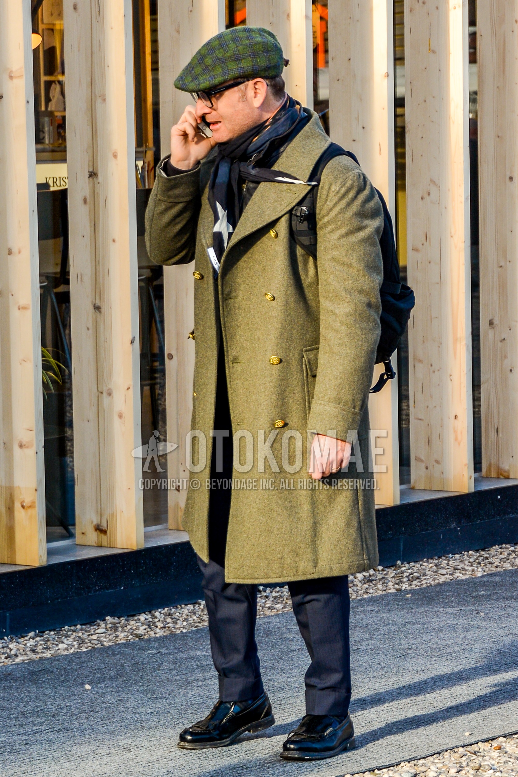 Men's winter outfit with green check cap, black plain glasses, navy scarf scarf, olive green plain ulster coat, gray plain slacks, blue socks socks, black  loafers leather shoes.