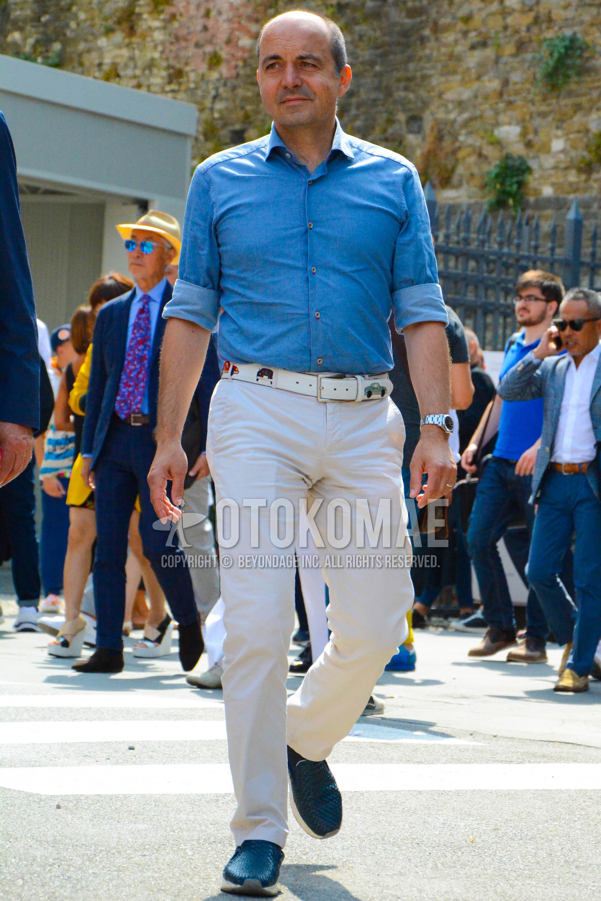Men's spring summer outfit with blue plain denim shirt/chambray shirt, white one point leather belt, beige plain chinos, navy low-cut sneakers.
