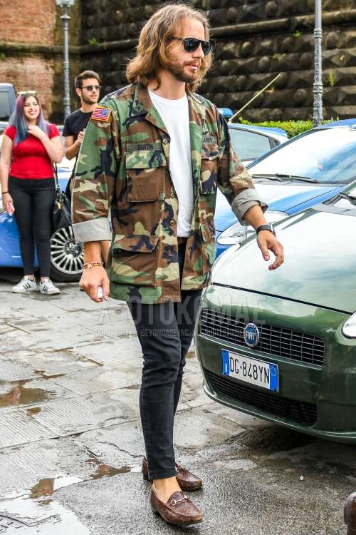 黒無地のサングラス、オリーブグリーン・ブラウン迷彩のM-65、白無地のTシャツ、ブラウン無地のレザーベルト、ダークグレー無地のデニム/ジーンズ、ブラウンビットローファーの革靴を合わせた春秋のメンズコーデ・着こなし。