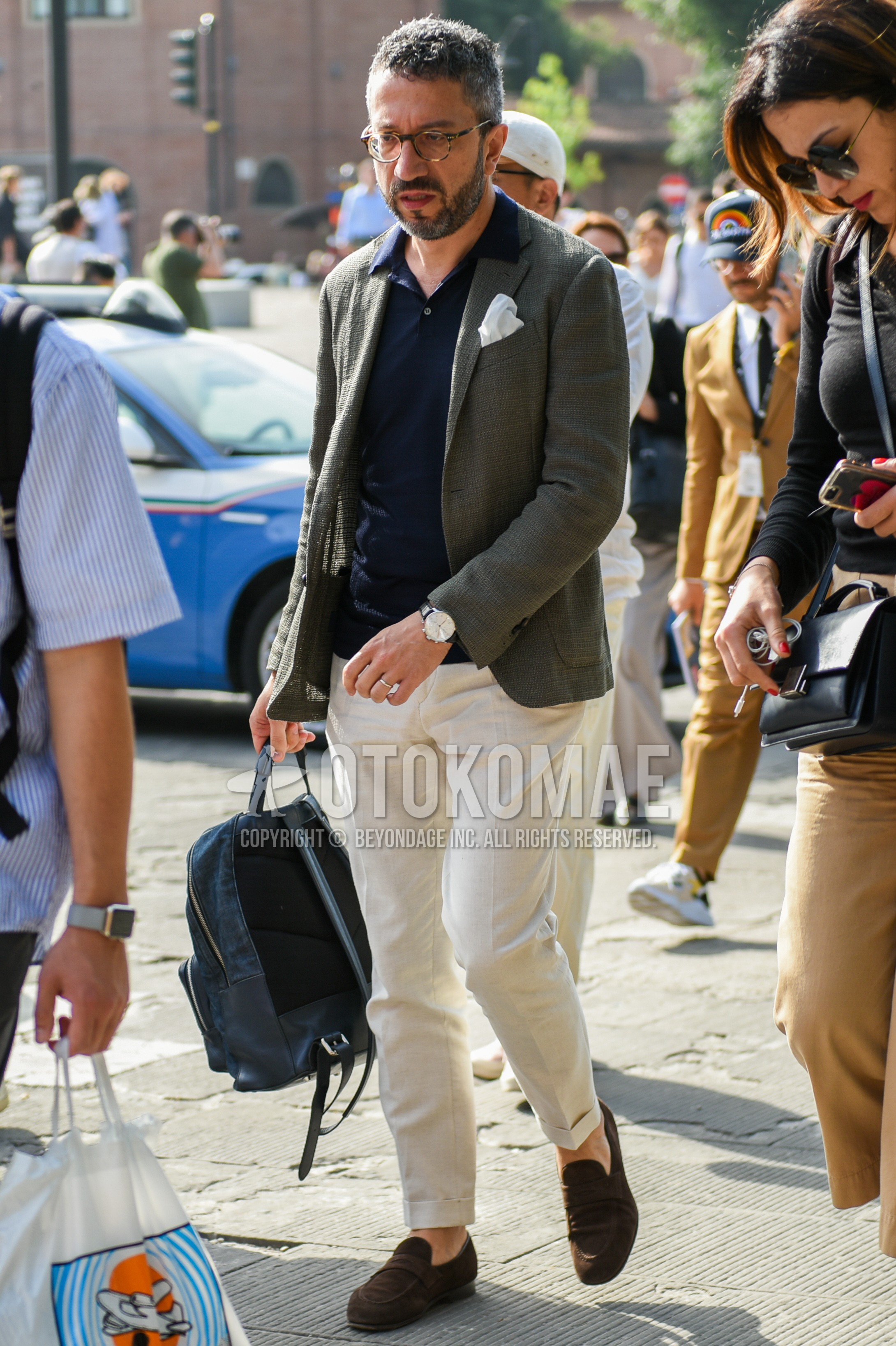 Men's spring summer autumn outfit with brown tortoiseshell glasses, olive green plain tailored jacket, navy plain polo shirt, white plain slacks, brown coin loafers leather shoes.