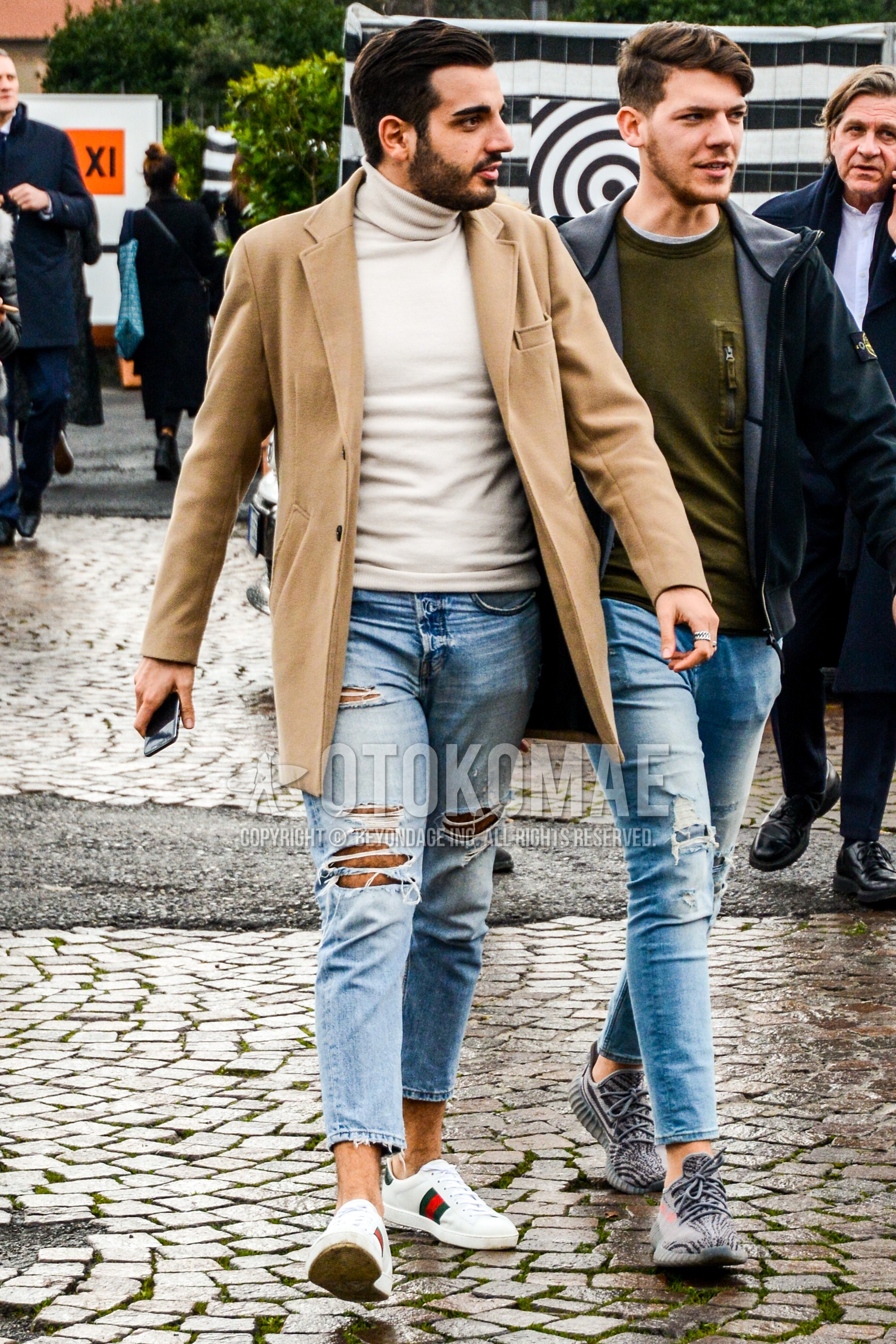 Men's autumn winter outfit with beige plain chester coat, white plain turtleneck knit, light blue plain damaged jeans, white low-cut sneakers.