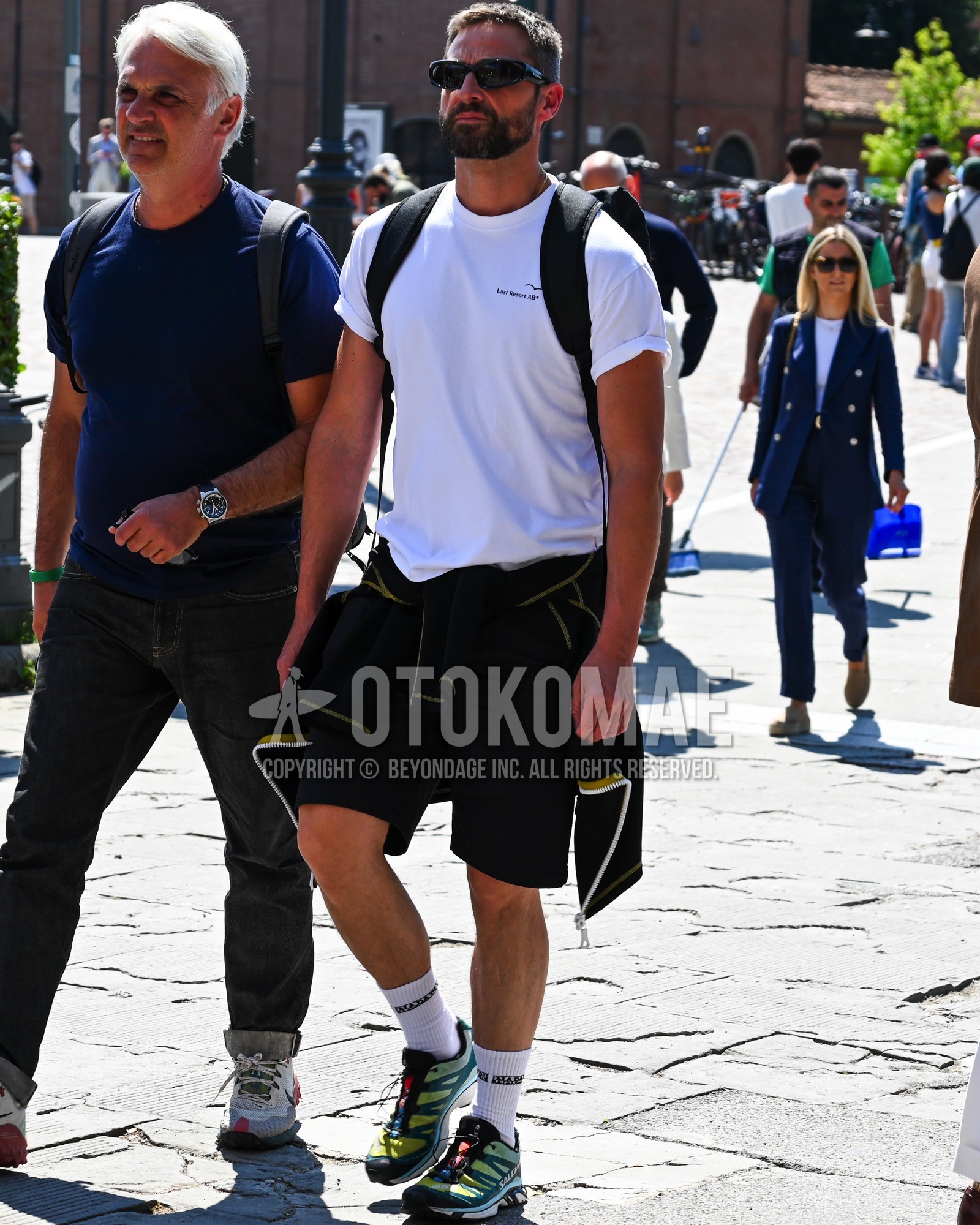 Men's spring summer outfit with black plain sunglasses, white one point t-shirt, black plain short pants, white one point socks, green low-cut sneakers, black plain backpack.