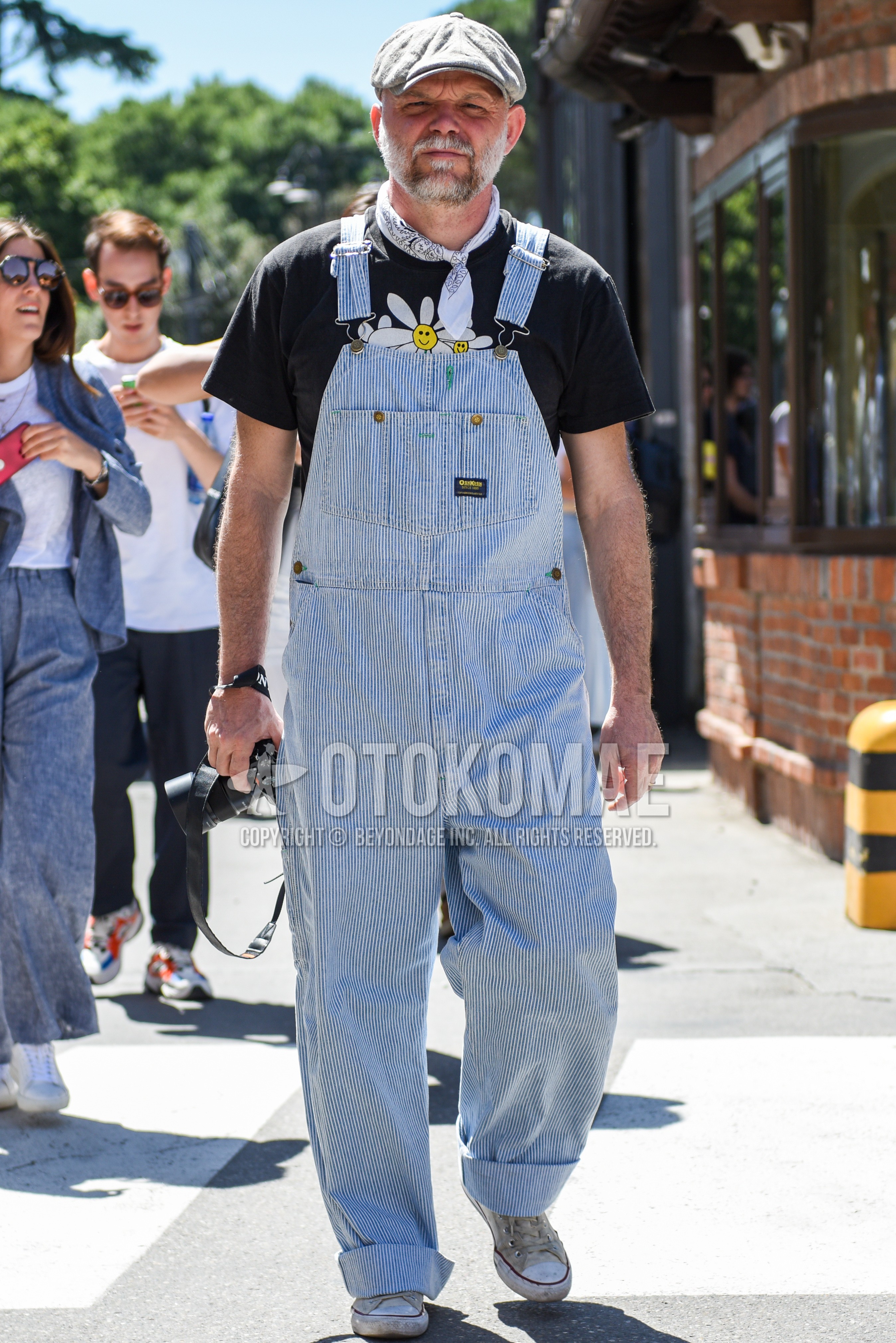 Men's spring summer outfit with gray plain cap, white scarf bandana/neckerchief, light blue stripes jumpsuit, black graphic t-shirt, white high-cut sneakers.