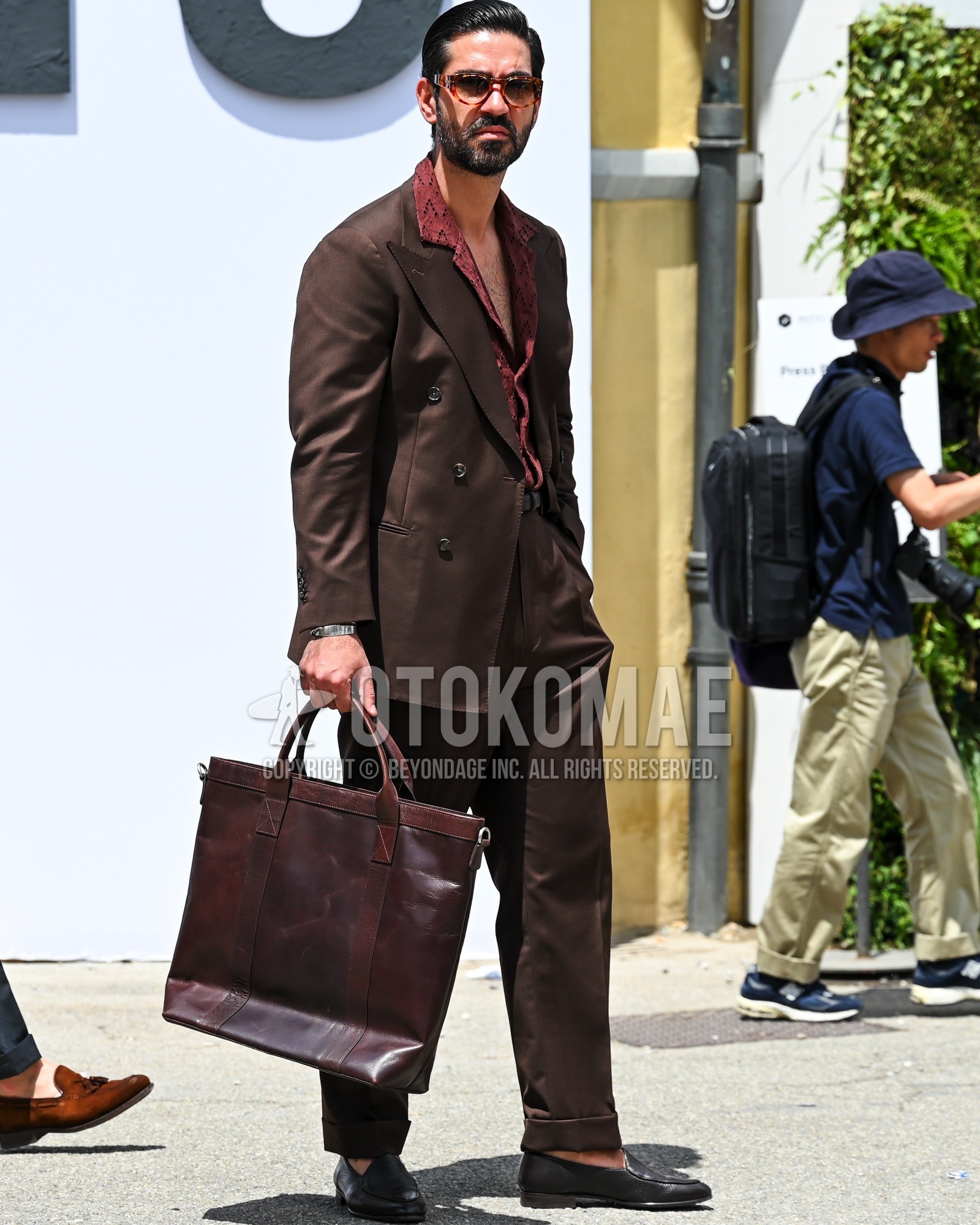 Men's spring summer autumn outfit with black tortoiseshell sunglasses, brown whole pattern shirt, brown plain socks, black  loafers leather shoes, brown plain tote bag, brown plain suit.