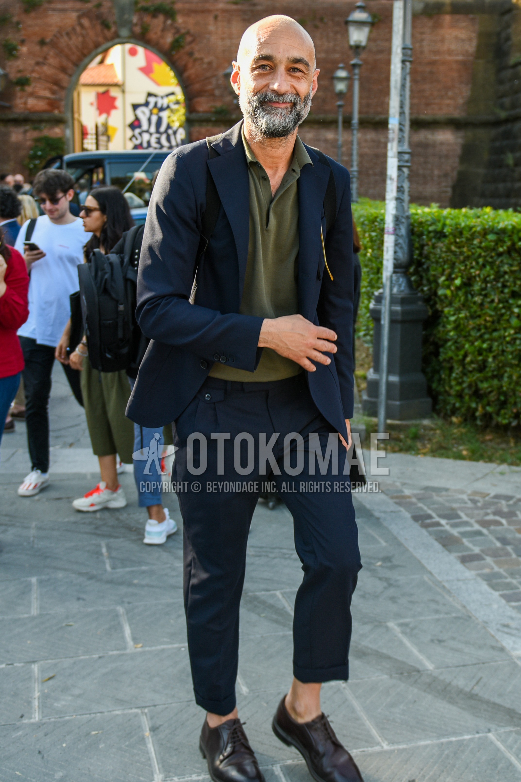 Men's spring summer autumn outfit with olive green plain polo shirt, brown plain toe leather shoes, navy plain suit.