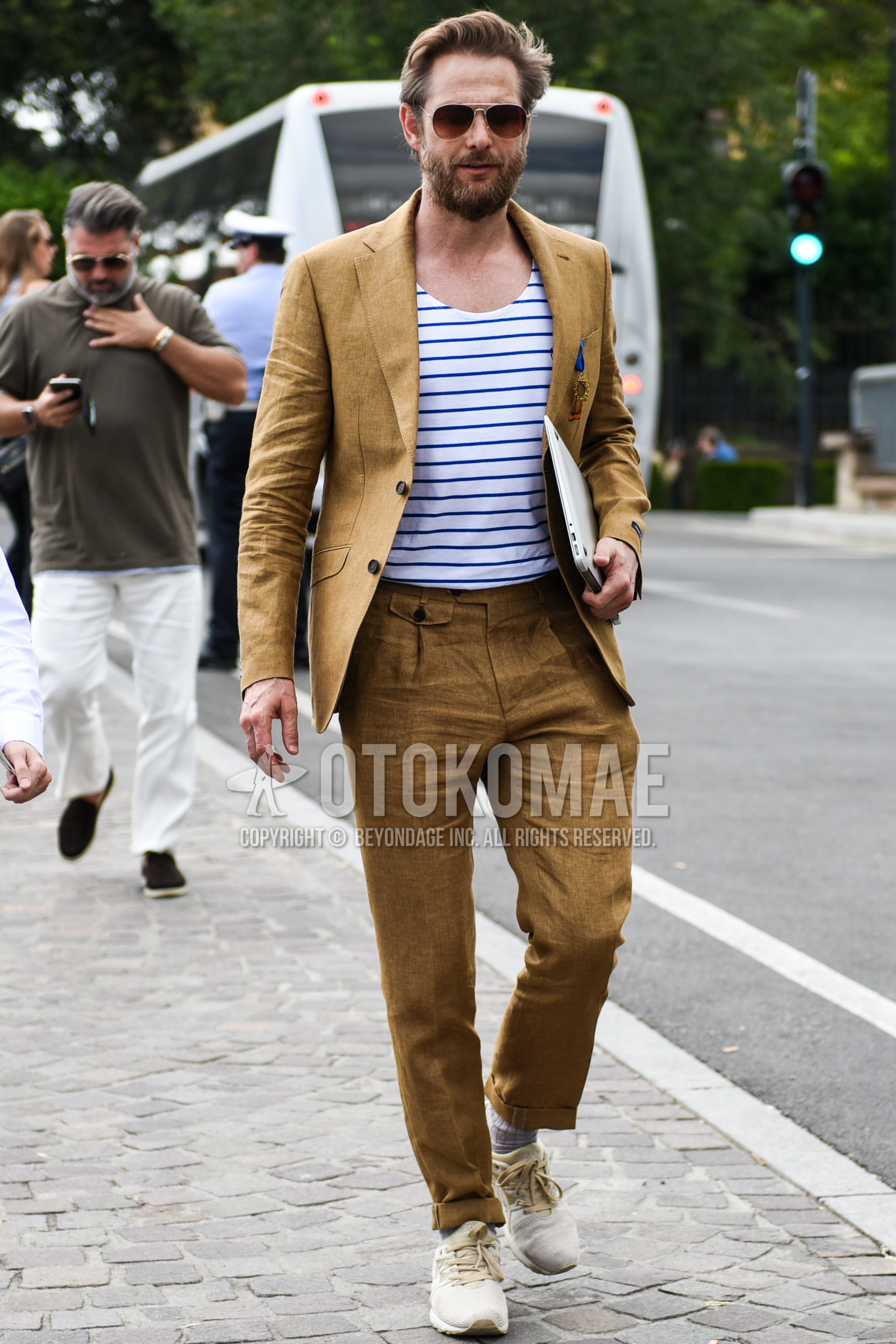 Men's spring summer outfit with brown plain sunglasses, brown plain tailored jacket, white blue horizontal stripes t-shirt, brown plain ankle pants, brown plain beltless pants, brown plain slacks, gray stripes socks, beige low-cut sneakers.
