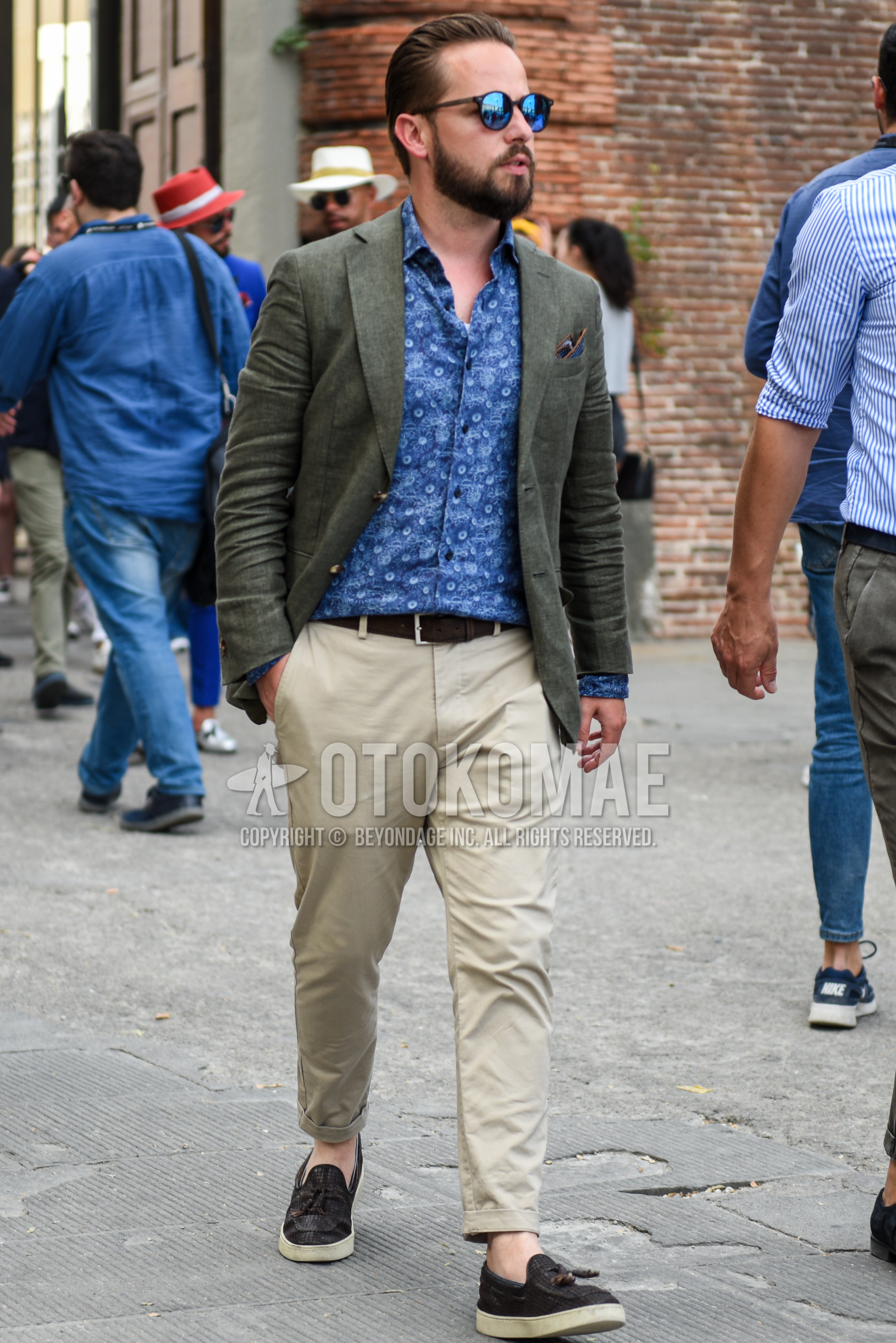 Men's spring summer autumn outfit with black plain sunglasses, olive green plain tailored jacket, blue tops/innerwear shirt, brown plain leather belt, beige plain chinos, brown low-cut sneakers.