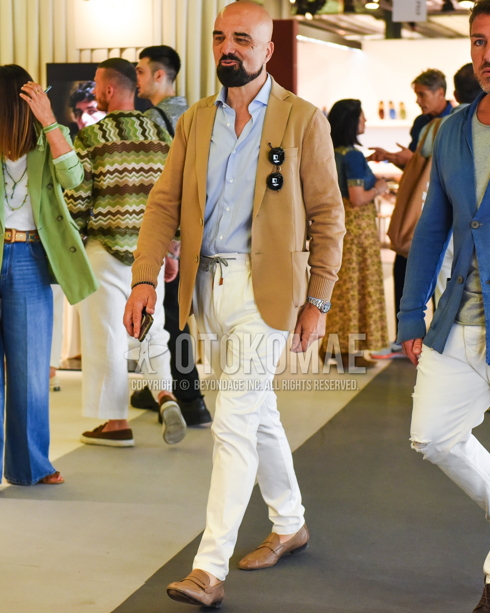Men's spring summer outfit with beige plain tailored jacket, blue plain shirt, white plain easy pants, brown coin loafers leather shoes.