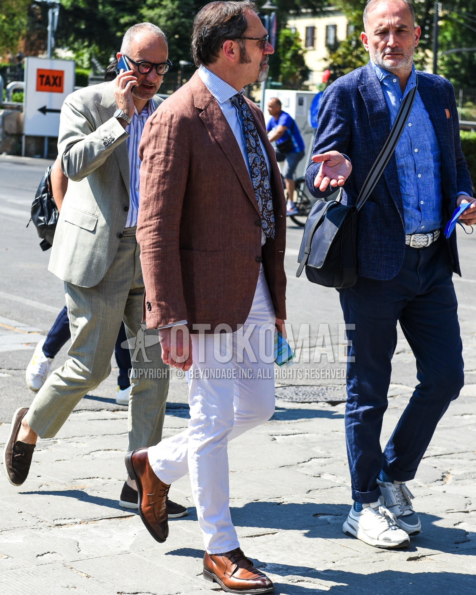 Men's spring summer outfit with brown tortoiseshell sunglasses, blue stripes tailored jacket, white plain cotton pants, brown u-tip shoes leather shoes, brown paisley necktie.