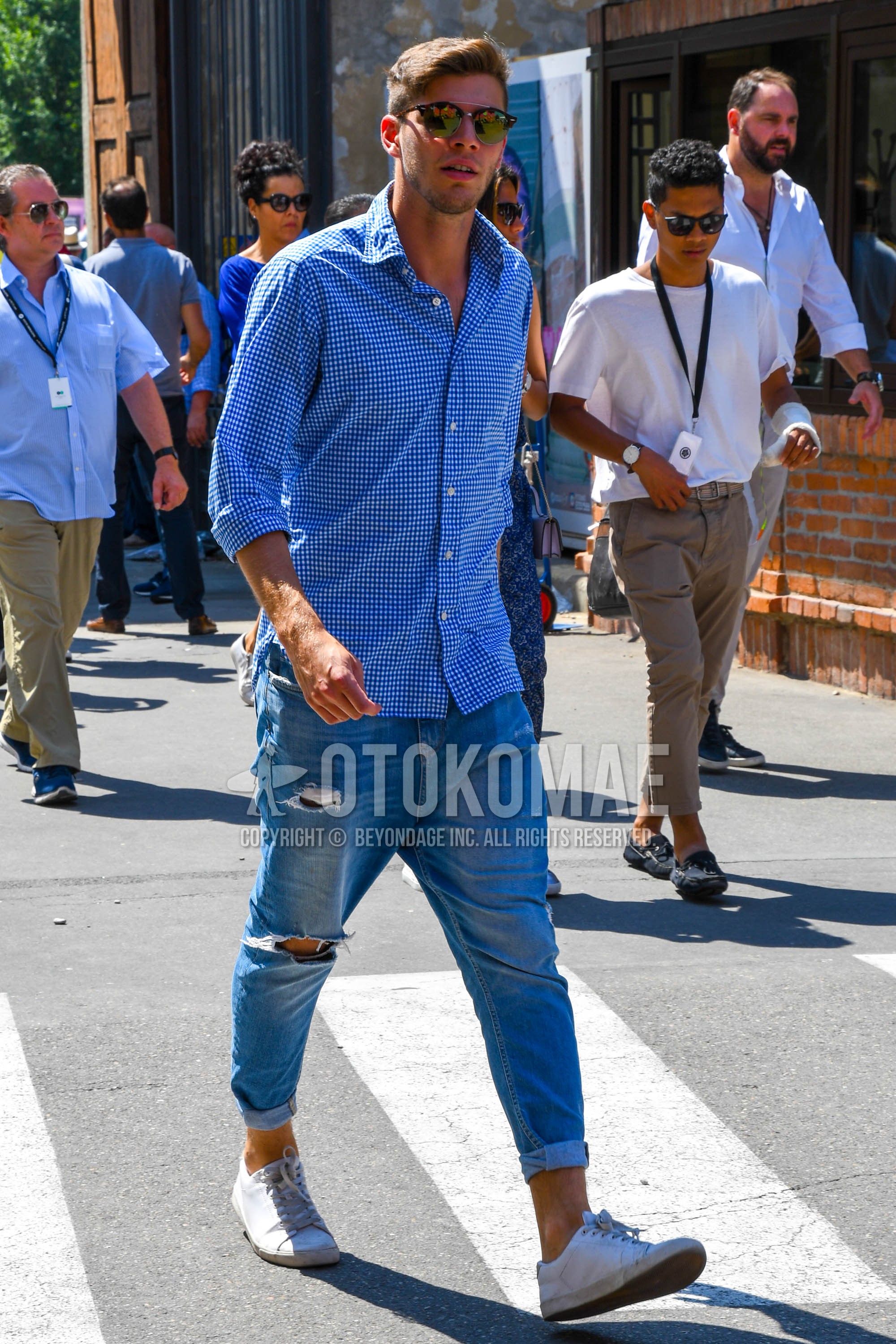 Men's spring summer outfit with brown tortoiseshell sunglasses, blue check shirt, blue plain damaged jeans, white low-cut sneakers.