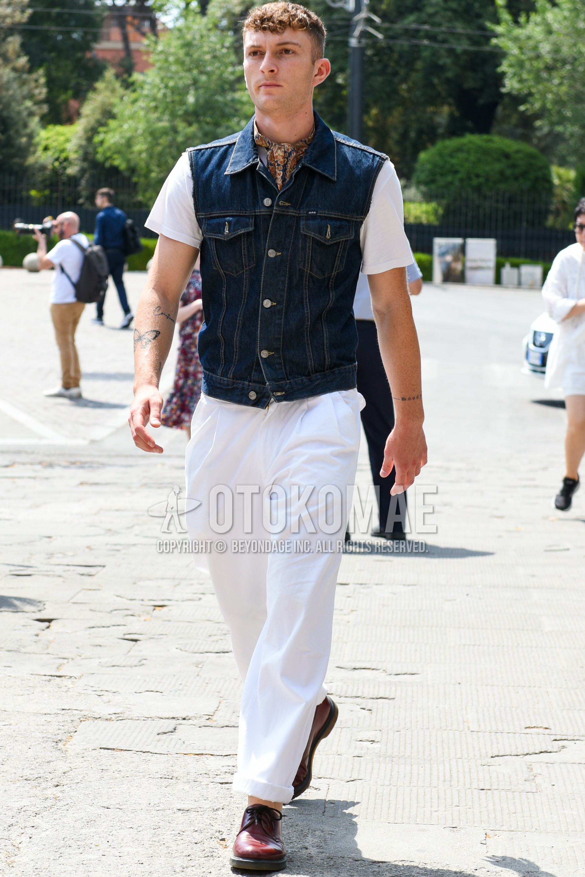 Men's spring summer outfit with brown scarf scarf, blue plain casual vest, white plain t-shirt, white plain cotton pants, white plain chinos, red plain toe leather shoes.