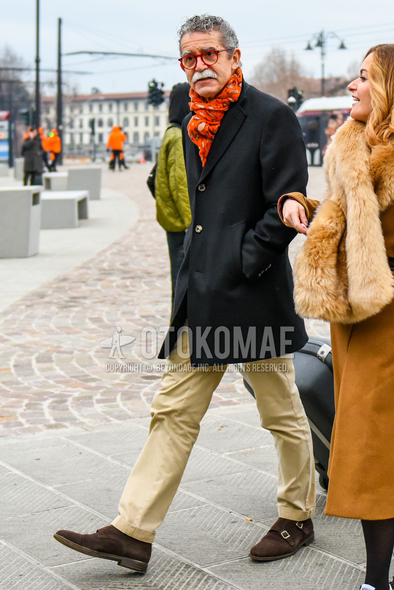 Men's autumn winter outfit with red plain glasses, orange scarf scarf, black plain chester coat, beige plain chinos, brown monk shoes leather shoes.