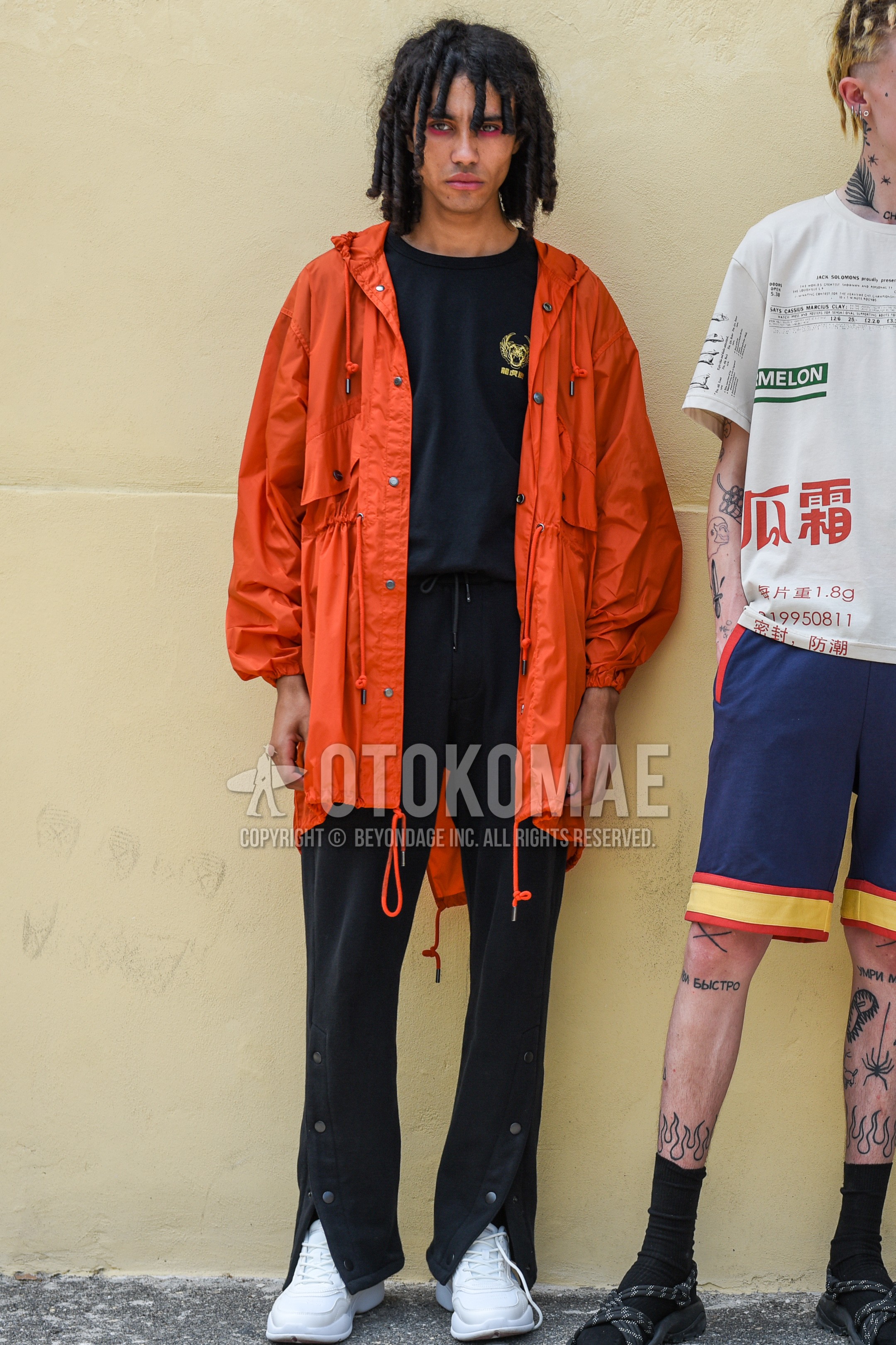 Men's spring autumn outfit with orange plain hooded coat, black one point t-shirt, black plain bottoms, white low-cut sneakers.