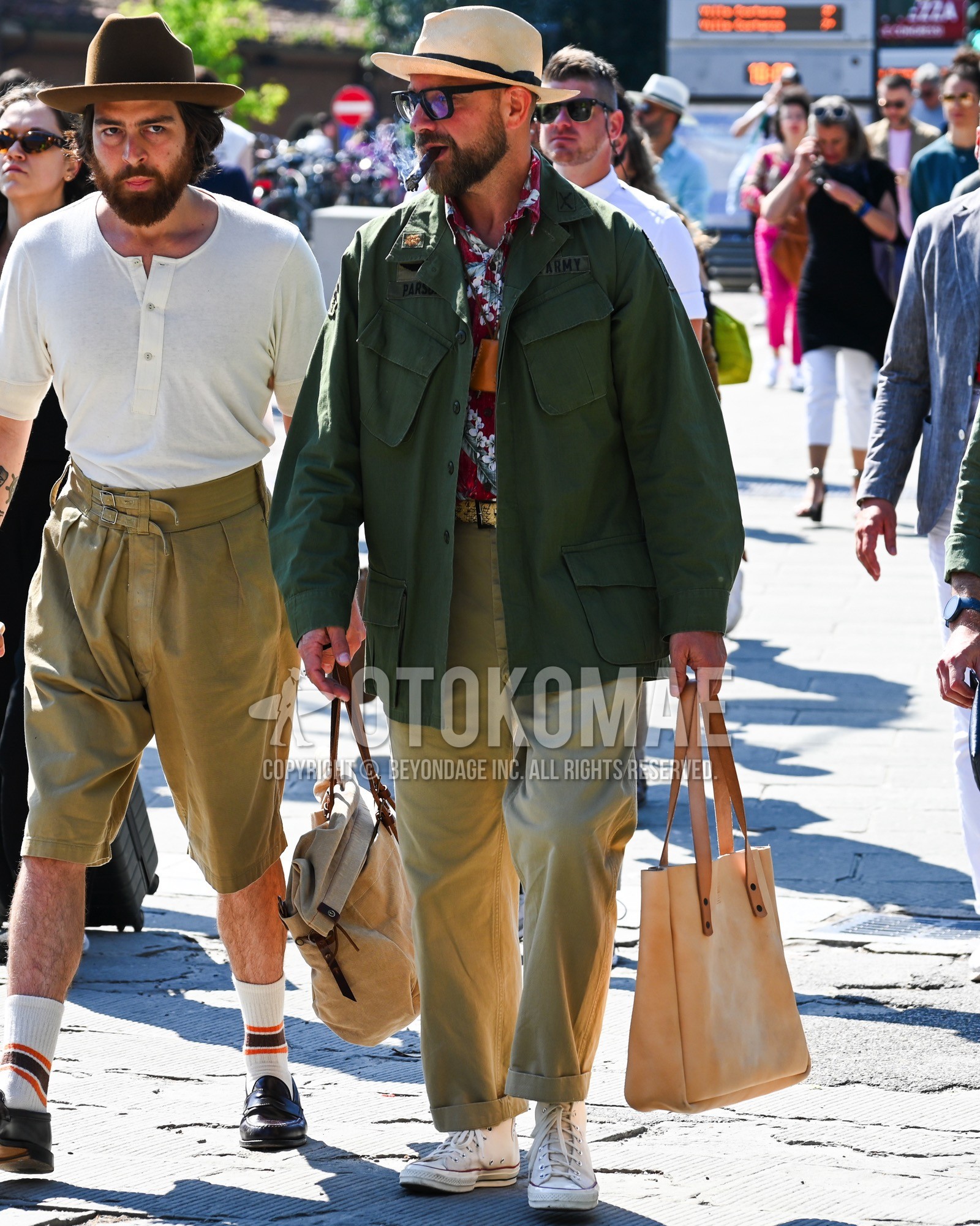 Men's spring summer autumn outfit with beige plain hat, blue plain sunglasses, olive green plain military jacket, red whole pattern shirt, beige plain chinos, white high-cut sneakers, brown plain tote bag.