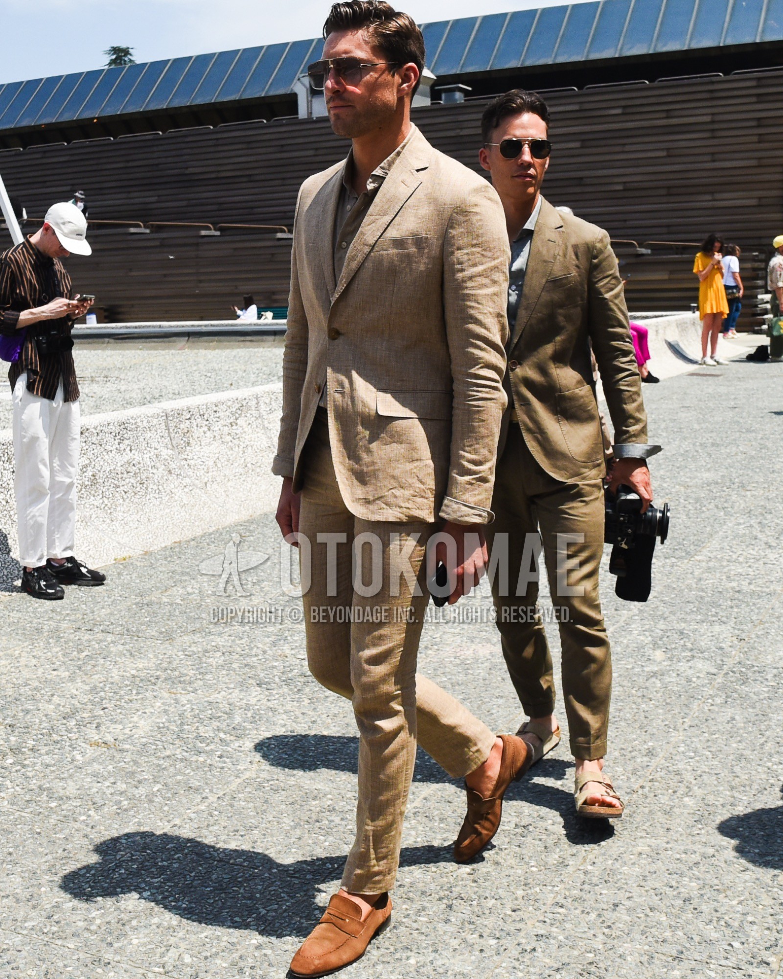 Men's spring summer outfit with brown plain sunglasses, beige plain shirt, brown coin loafers leather shoes, beige plain suit.