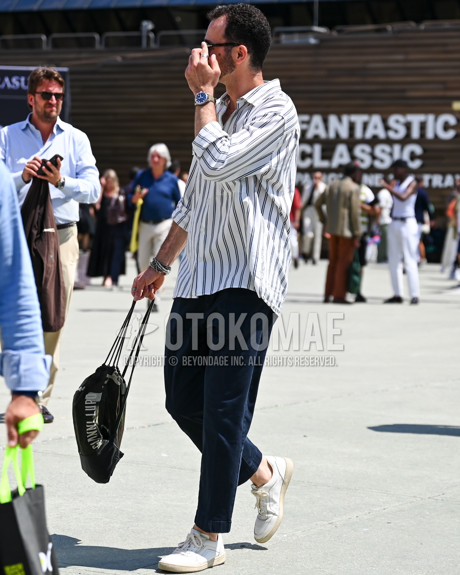 Men's spring summer autumn outfit with black plain sunglasses, white gray stripes shirt, navy plain slacks, white low-cut sneakers.