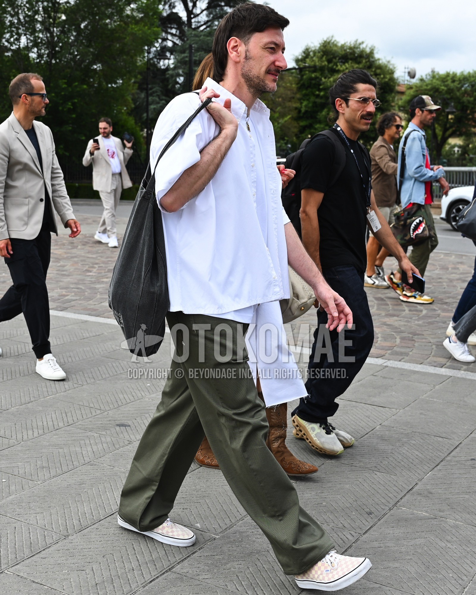 Men's spring summer outfit with white plain shirt, olive green plain chinos, beige low-cut sneakers, black plain clutch bag/second bag/drawstring bag.