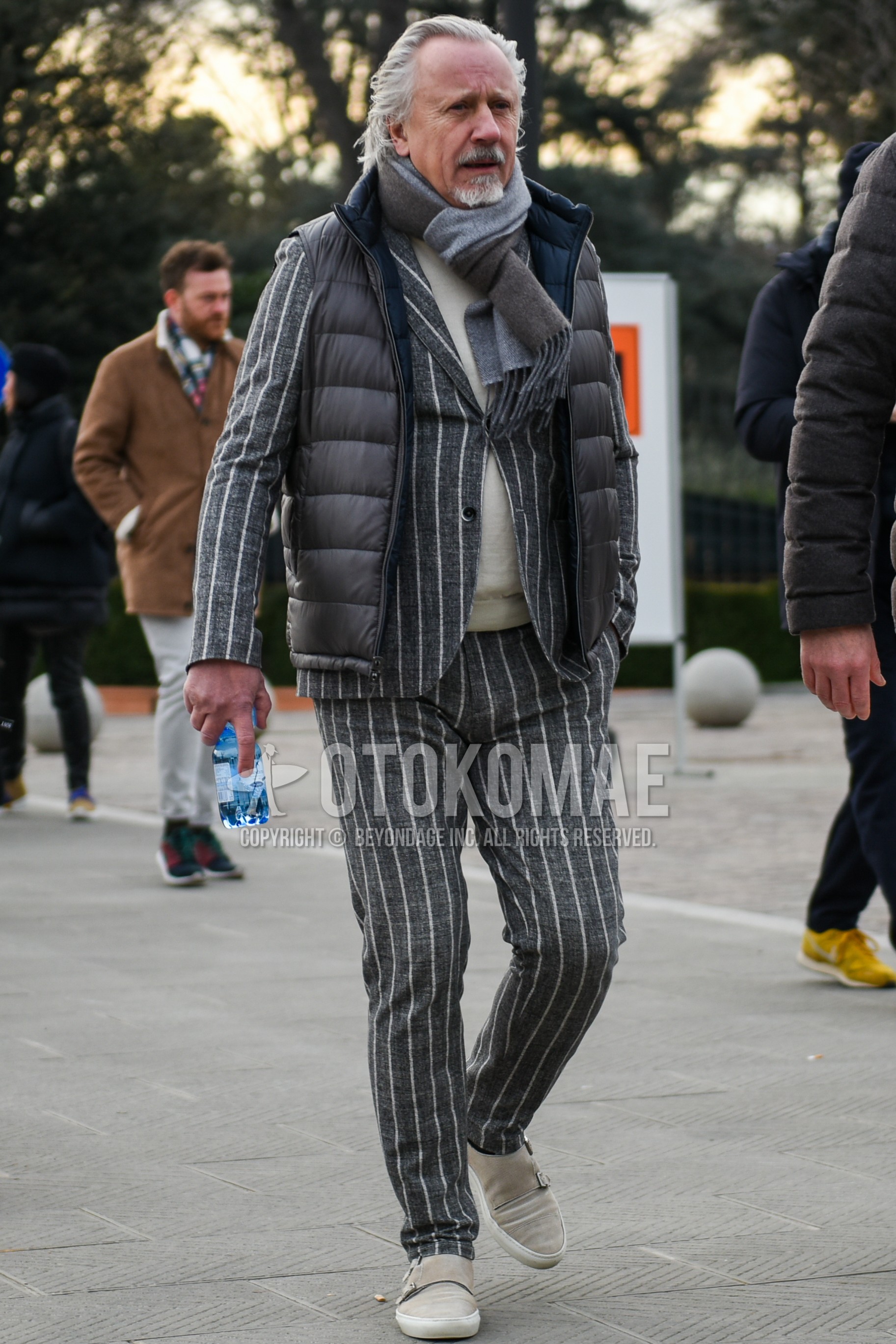 Men's autumn winter outfit with gray plain scarf, gray plain down jacket, white plain turtleneck knit, gray plain casual vest, beige low-cut sneakers, gray stripes suit.