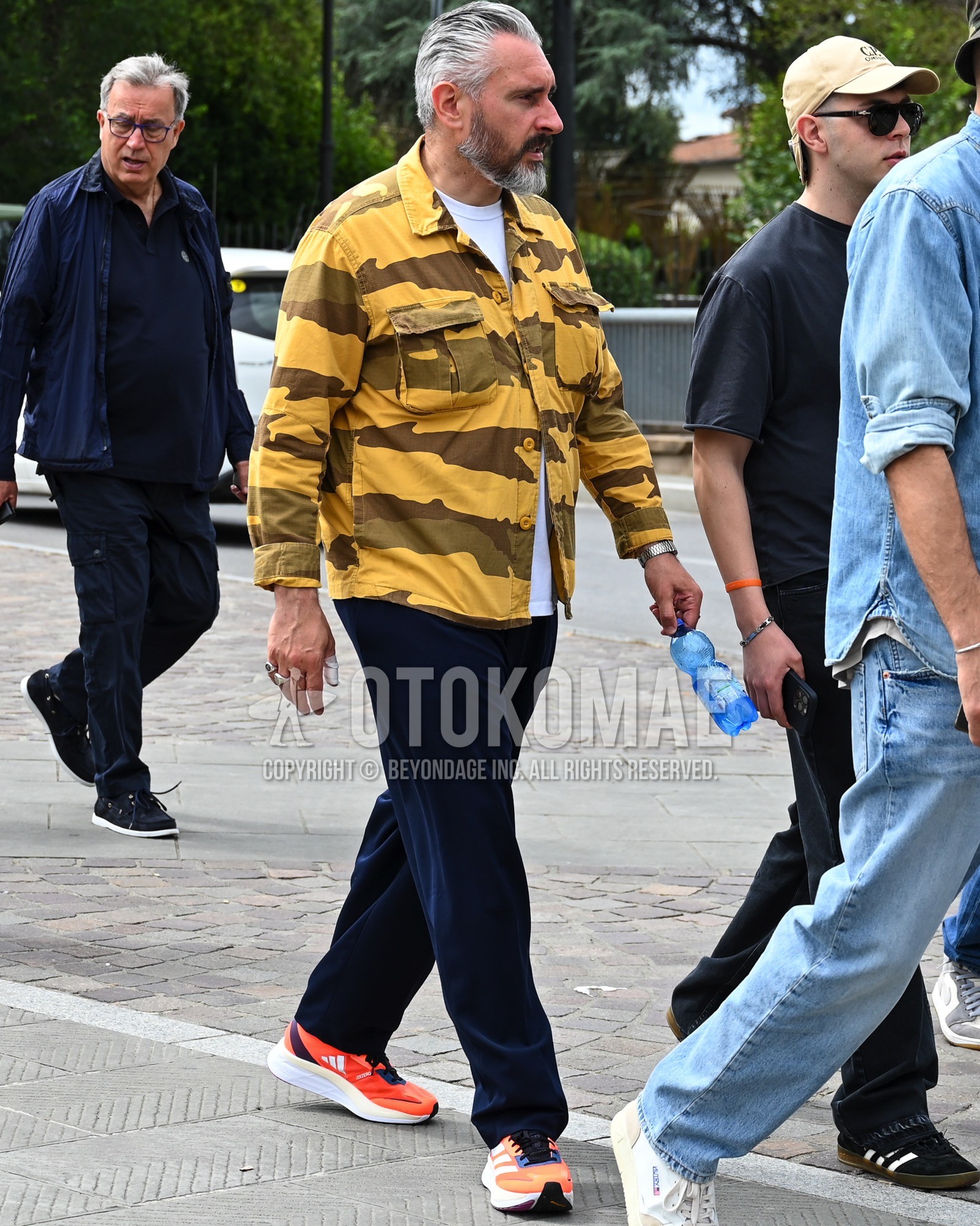 Men's spring summer autumn outfit with yellow camouflage military jacket, white plain t-shirt, navy plain chinos, orange low-cut sneakers.