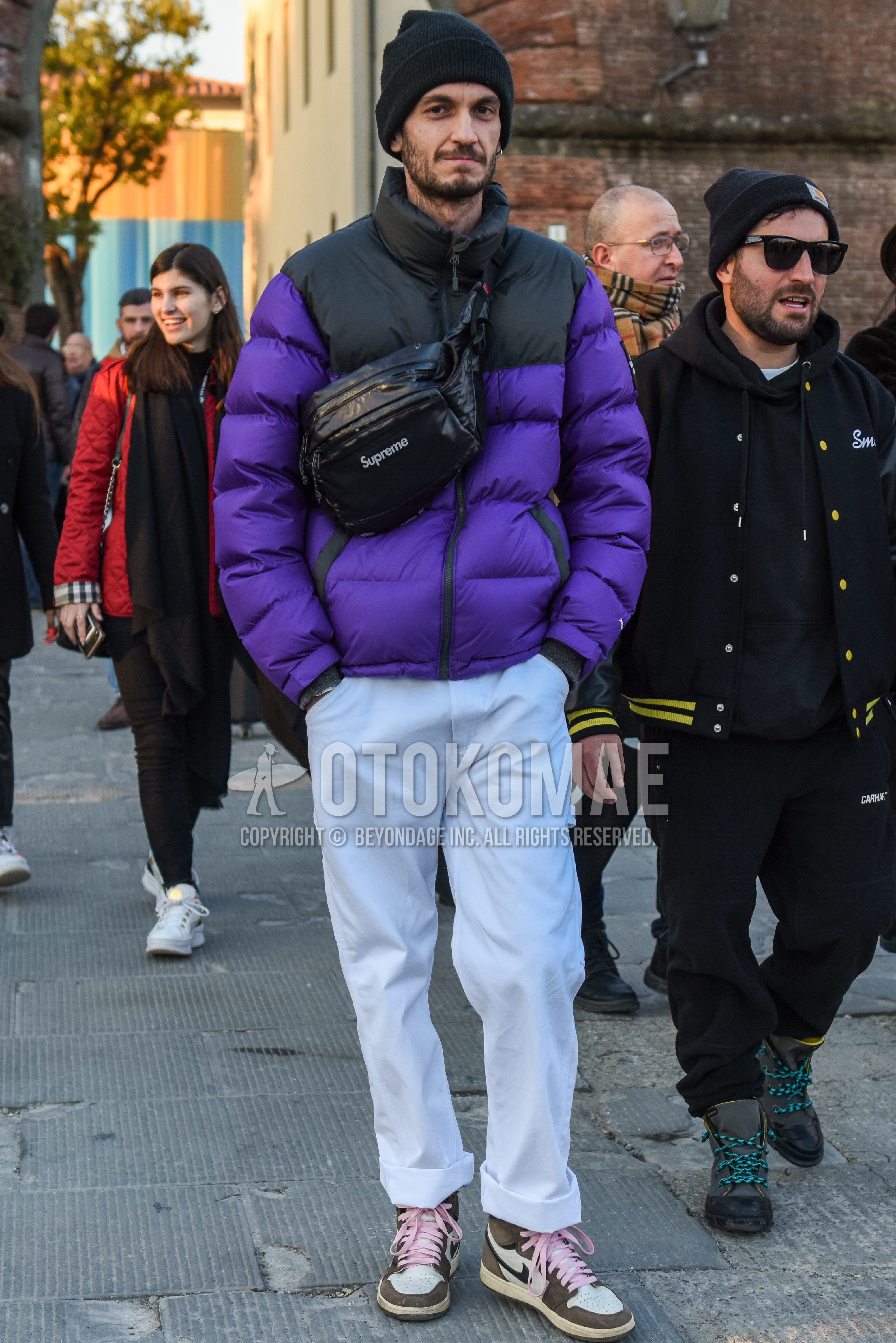 Men's autumn winter outfit with dark gray plain knit cap, black purple plain down jacket, white plain cotton pants, beige white high-cut sneakers, black one point shoulder bag.