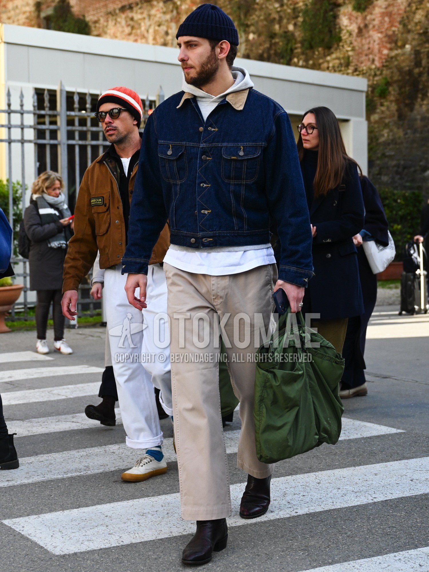 Men's autumn winter outfit with navy plain knit cap, beige plain trucker jacket, gray plain hoodie, white plain long sleeve t-shirt, beige plain chinos, brown  boots, olive green plain briefcase/handbag.