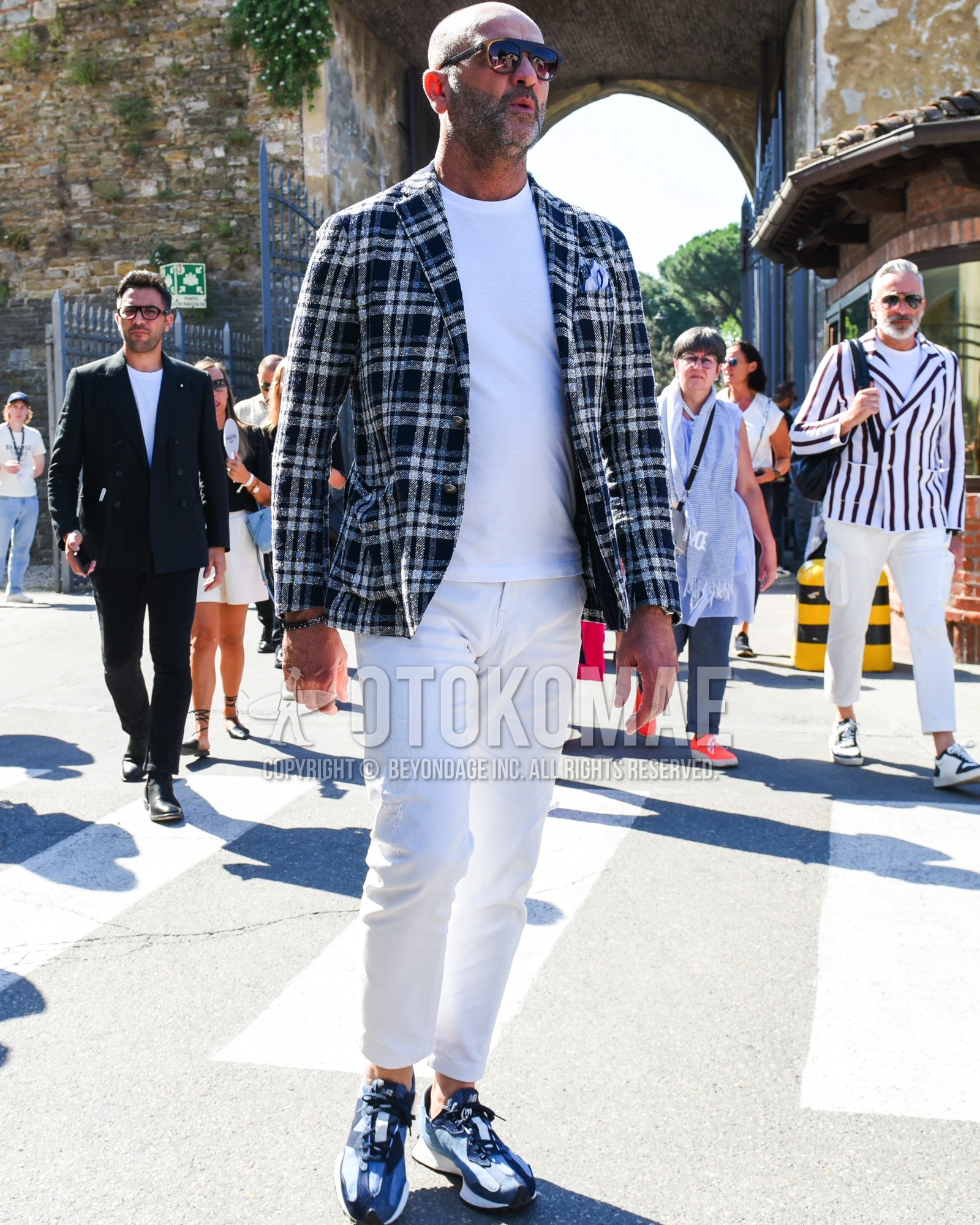 Men's spring summer outfit with brown plain sunglasses, dark gray check tailored jacket, white plain t-shirt, white plain cotton pants, white plain ankle pants, navy low-cut sneakers.