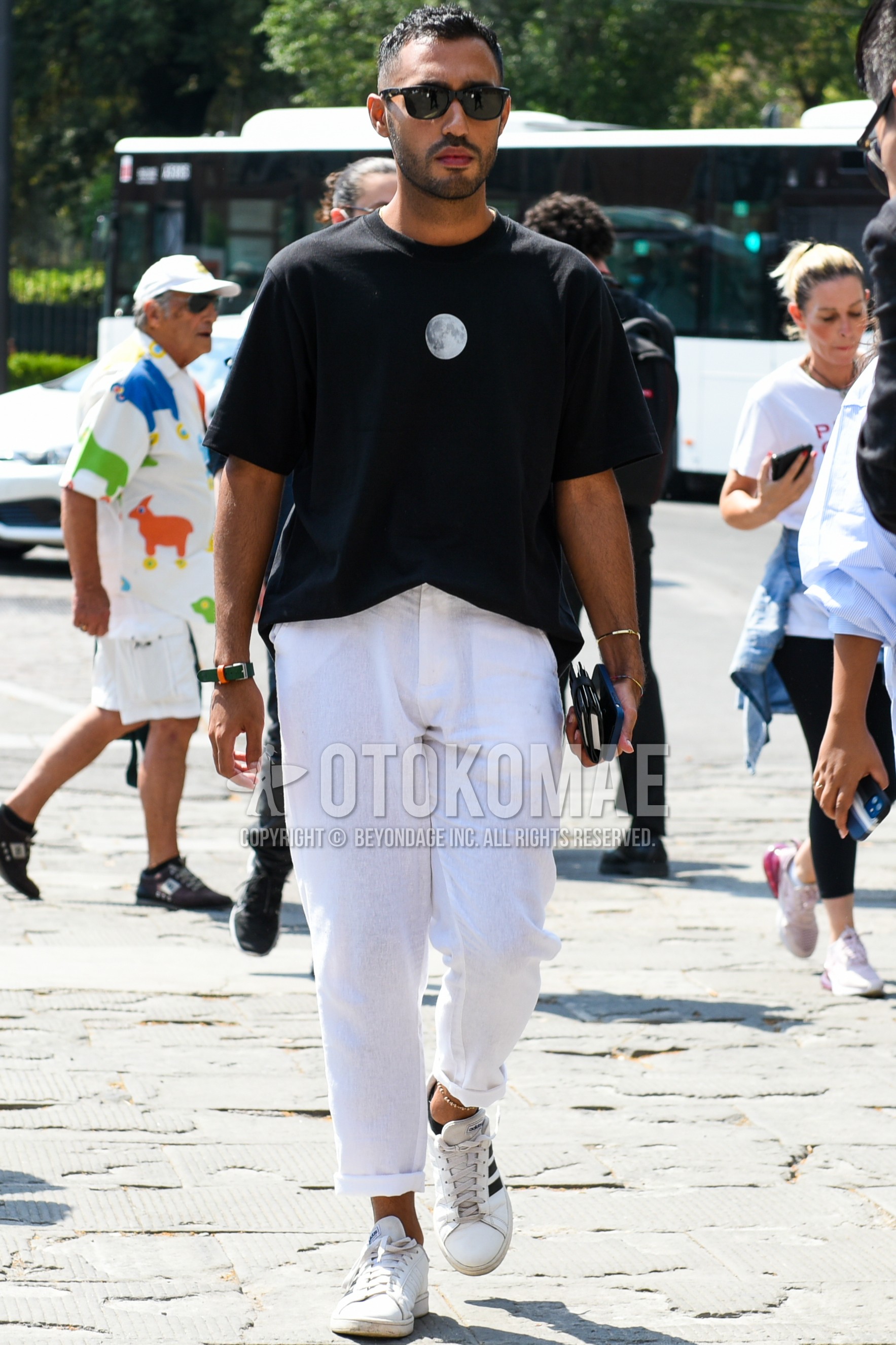 Men's spring summer outfit with black plain sunglasses, black plain t-shirt, white plain cotton pants, white low-cut sneakers.
