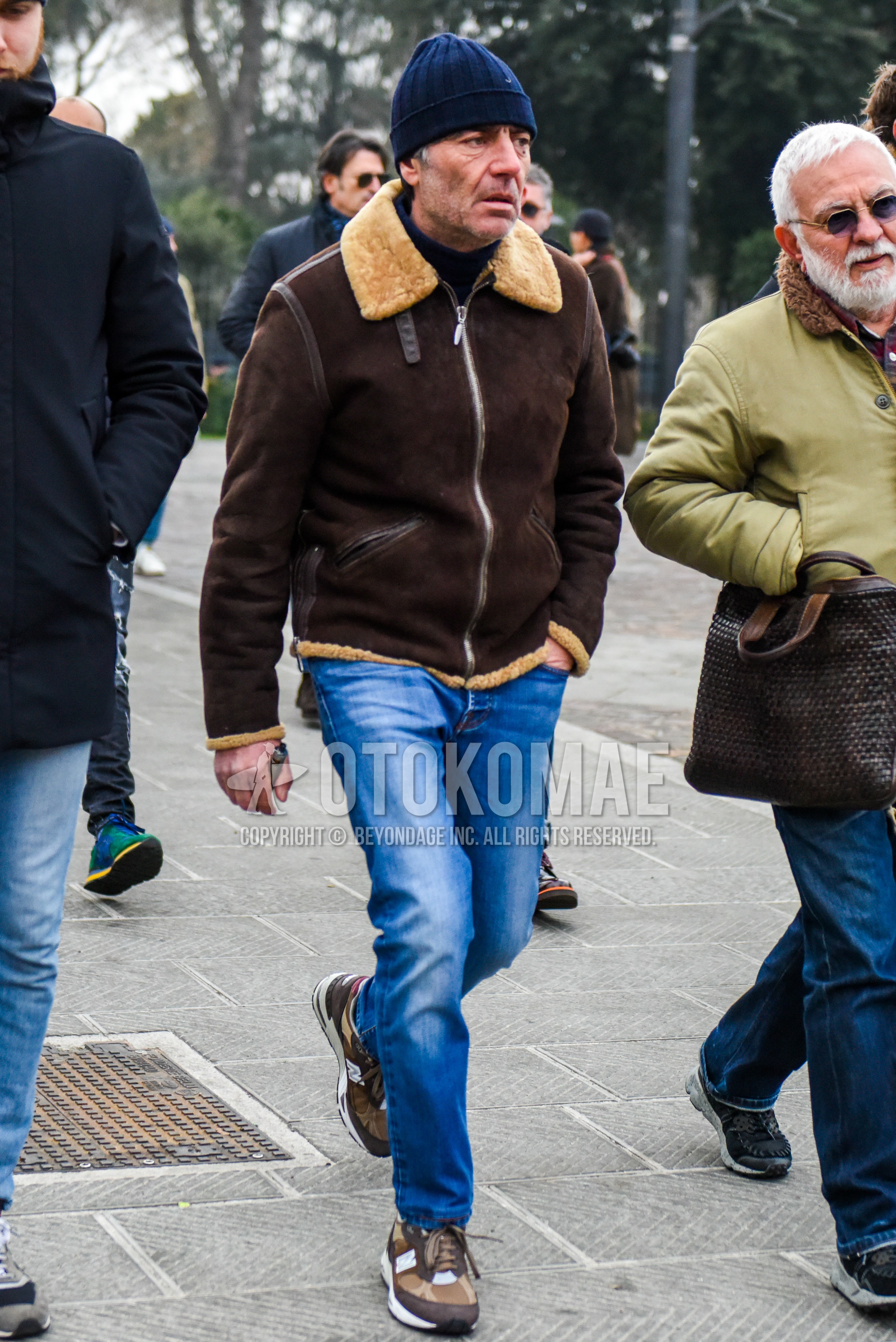 Men's winter outfit with navy plain knit cap, brown plain leather jacket, blue plain denim/jeans, brown low-cut sneakers.