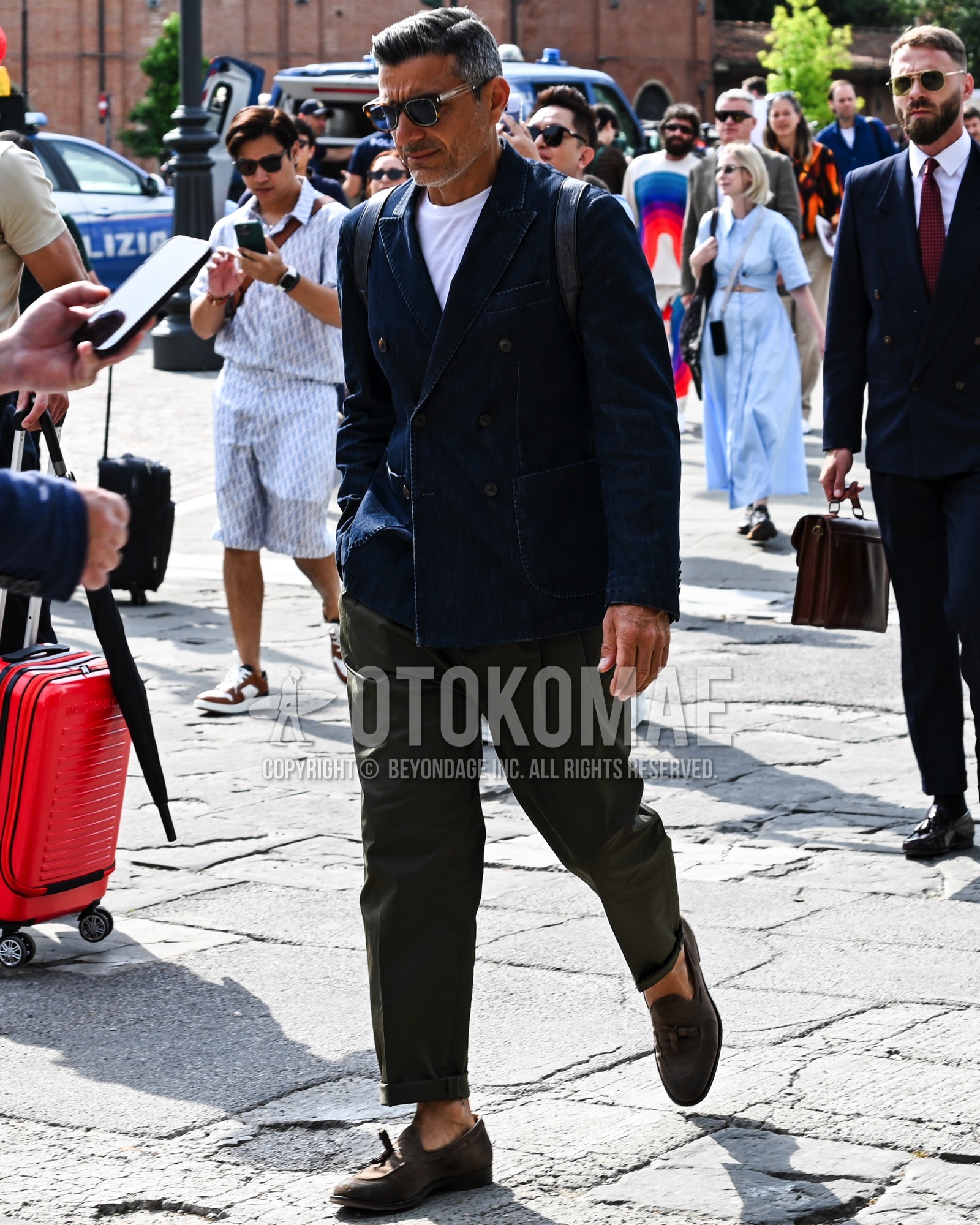 Men's spring summer autumn outfit with black plain sunglasses, navy plain tailored jacket, white plain t-shirt, olive green plain chinos, brown moccasins/deck shoes leather shoes, black plain backpack.