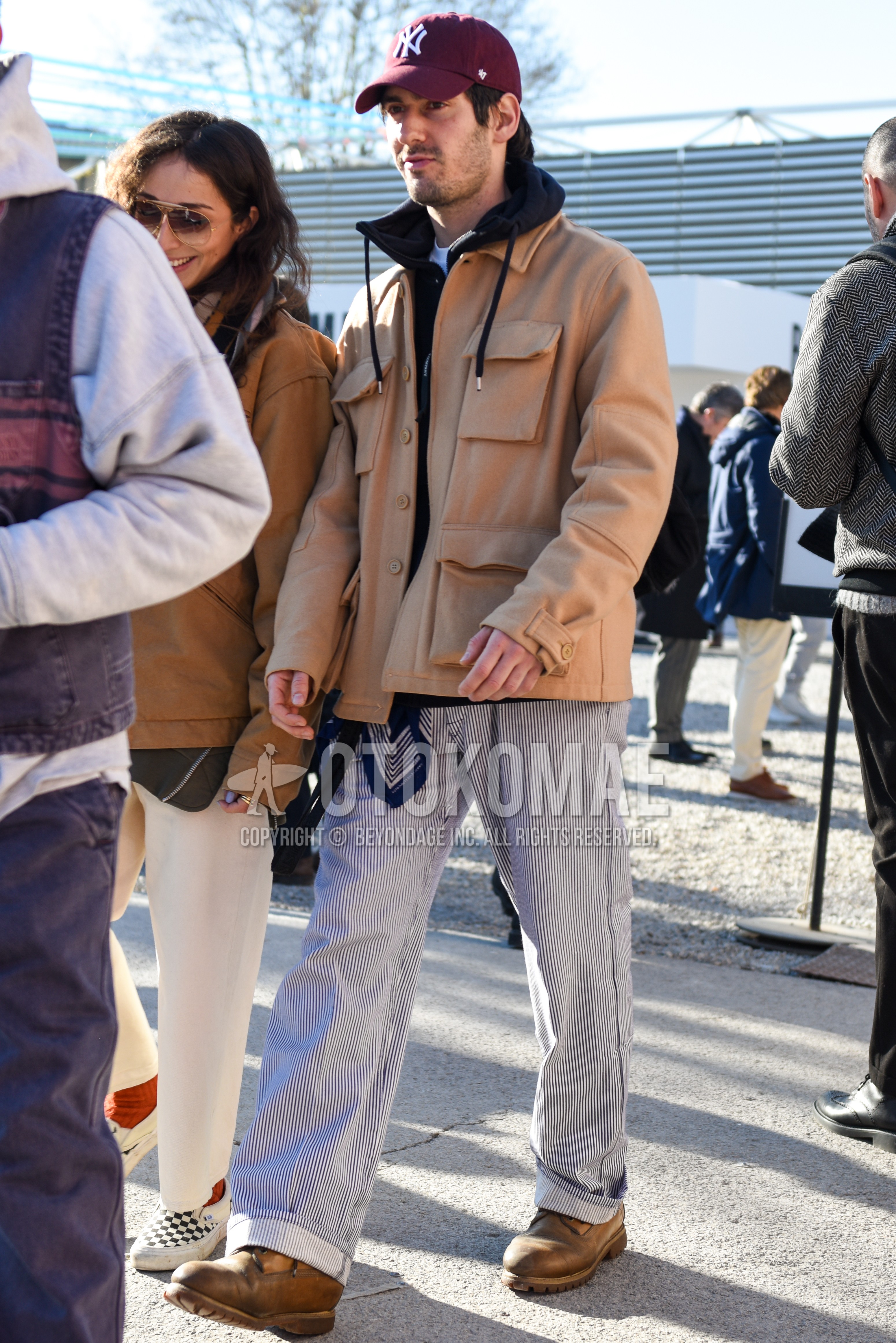 Men's autumn winter outfit with brown plain baseball cap, beige plain shirt jacket, black plain hoodie, blue stripes cotton pants, brown work boots.