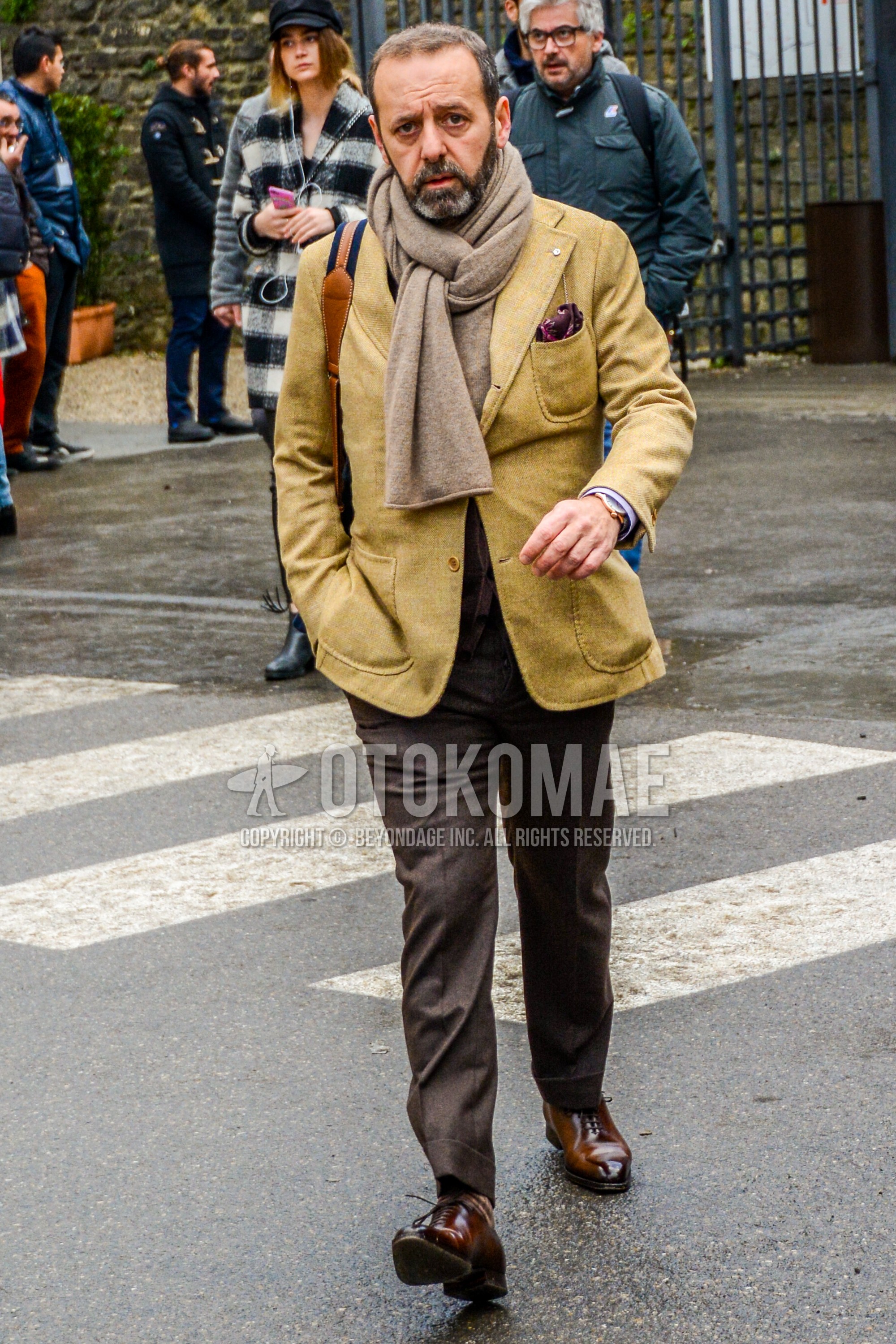 Men's winter outfit with brown plain scarf, yellow plain tailored jacket, brown plain slacks, brown plain toe leather shoes.
