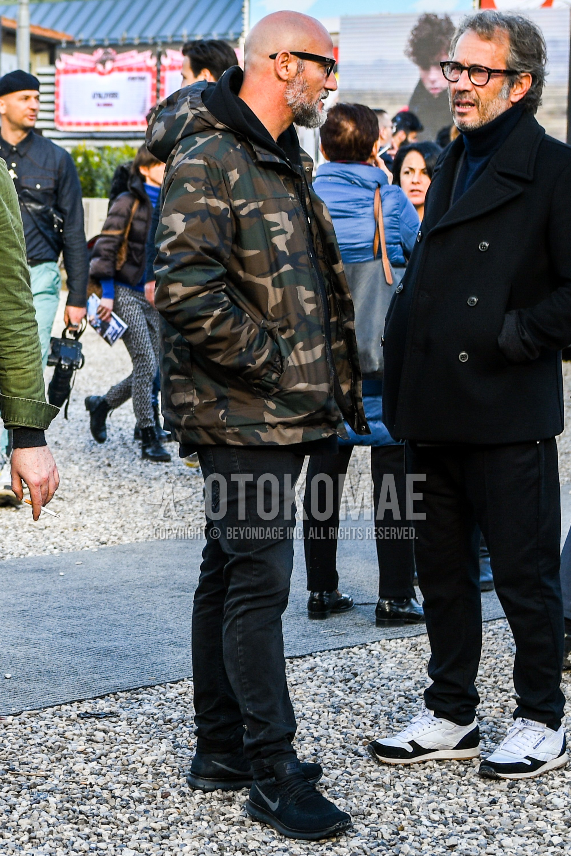 Men's autumn winter outfit with plain sunglasses, multi-color camouflage down jacket, black plain hoodie, black plain denim/jeans, black low-cut sneakers.