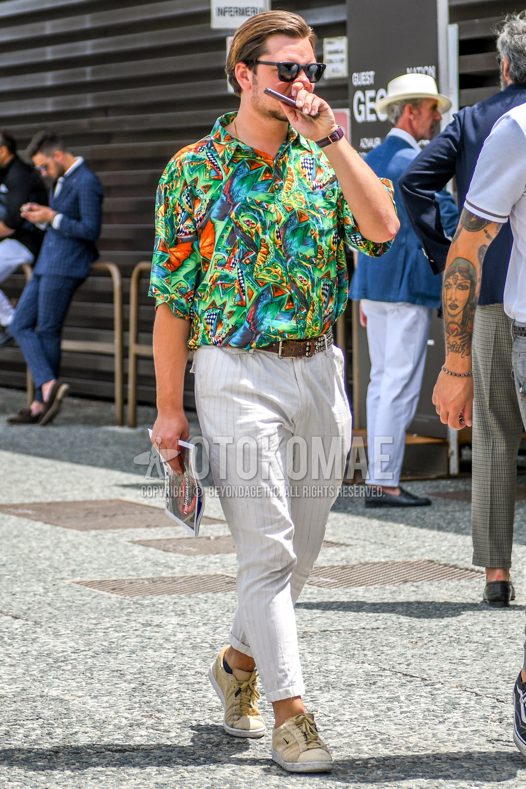Men's summer outfit with plain sunglasses, green tops/innerwear shirt, brown belt leather belt, white stripes ankle pants, beige low-cut sneakers.