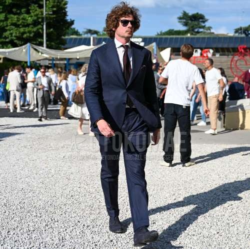 ペルソール 649の黒無地のサングラス、白無地のシャツ、ネイビープレーントゥの革靴、ネイビースエードシューズの革靴、ネイビー無地のスーツ、レッドネクタイのネクタイを合わせた春夏のメンズコーデ・着こなし。