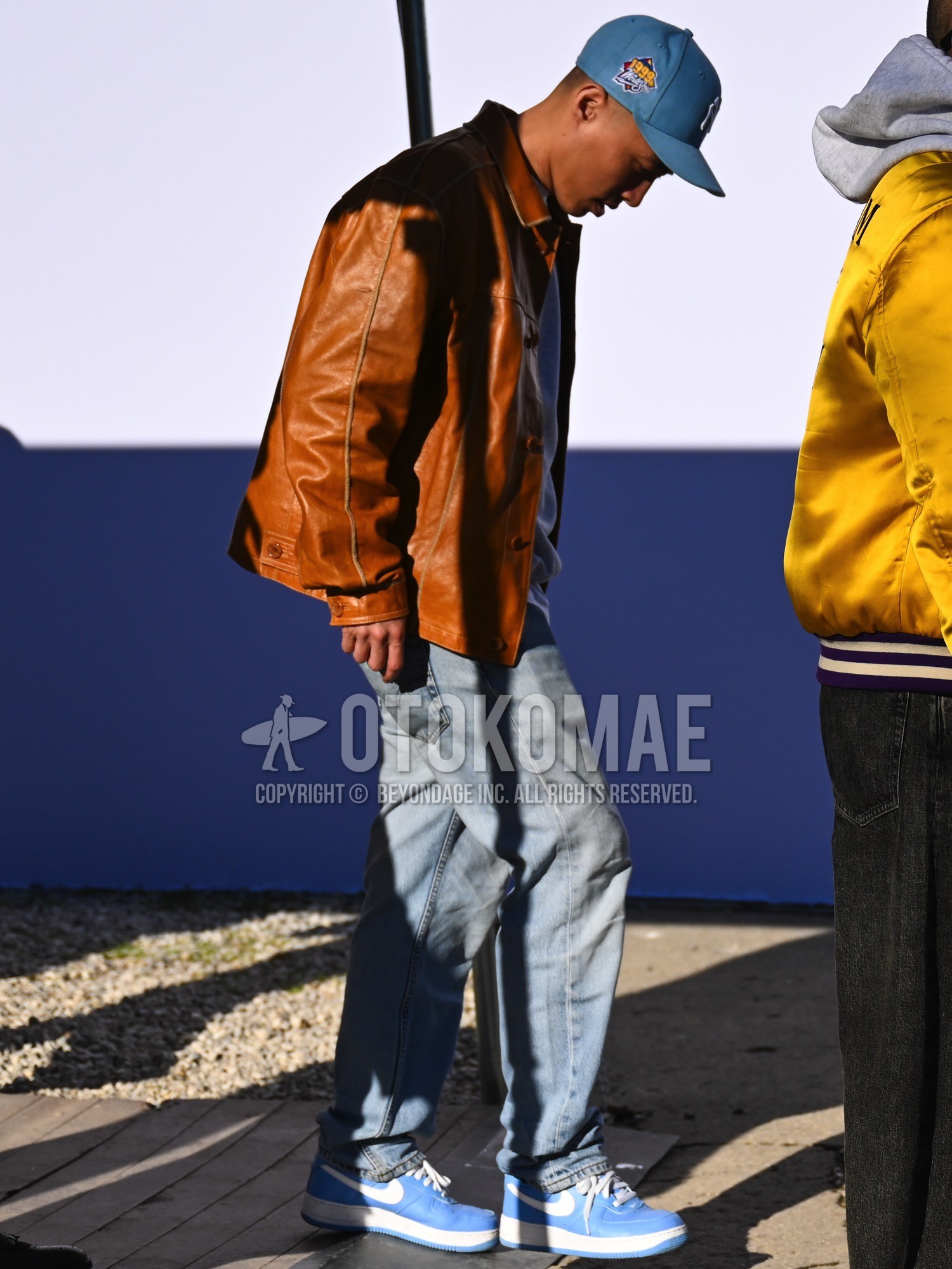 Men's spring autumn winter outfit with blue one point baseball cap, brown plain leather jacket, gray plain long sleeve t-shirt, blue plain denim/jeans, blue high-cut sneakers.