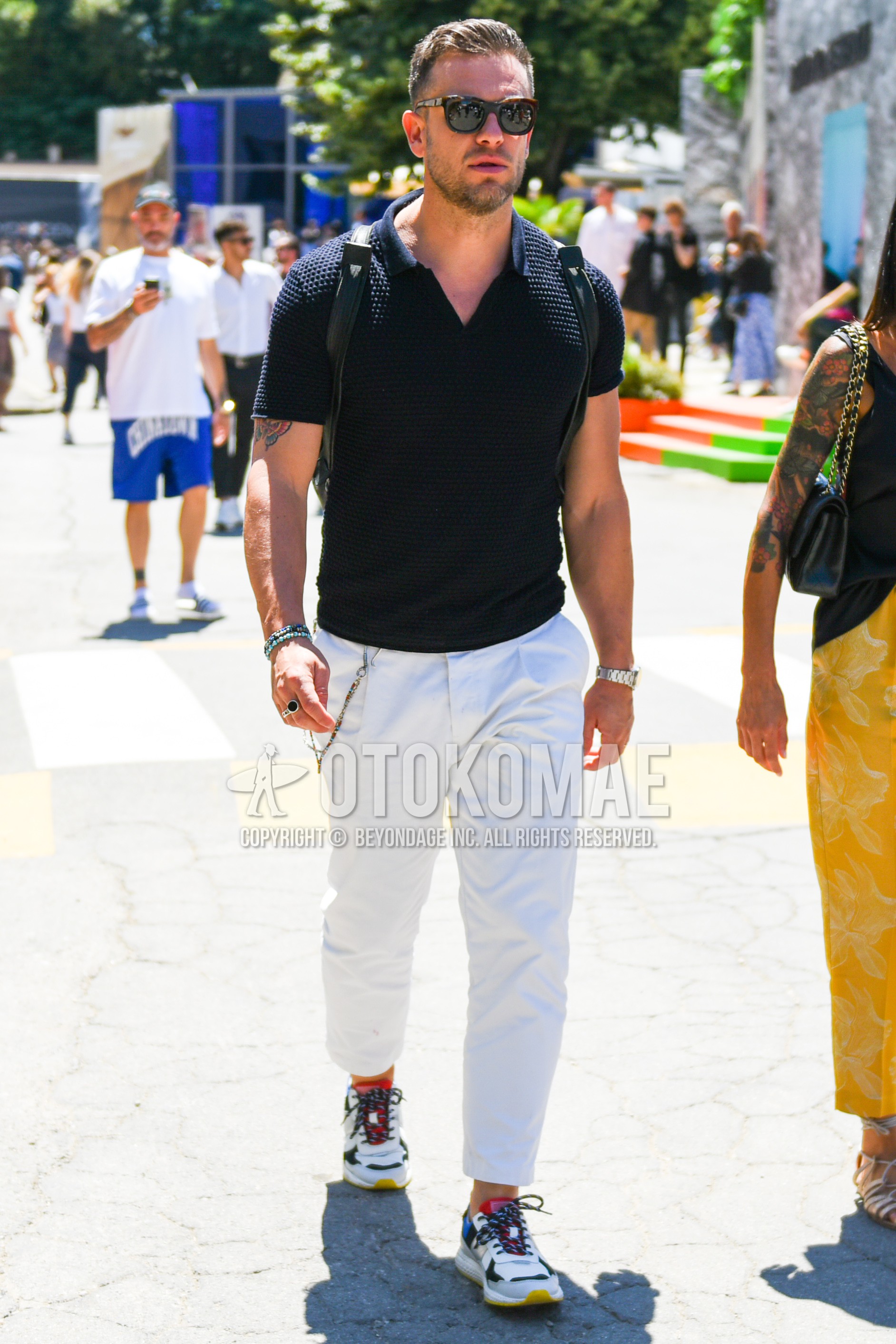 Men's spring summer outfit with brown tortoiseshell sunglasses, black plain polo shirt, white plain cotton pants, white plain cropped pants, white plain pleated pants, white multi-color low-cut sneakers.