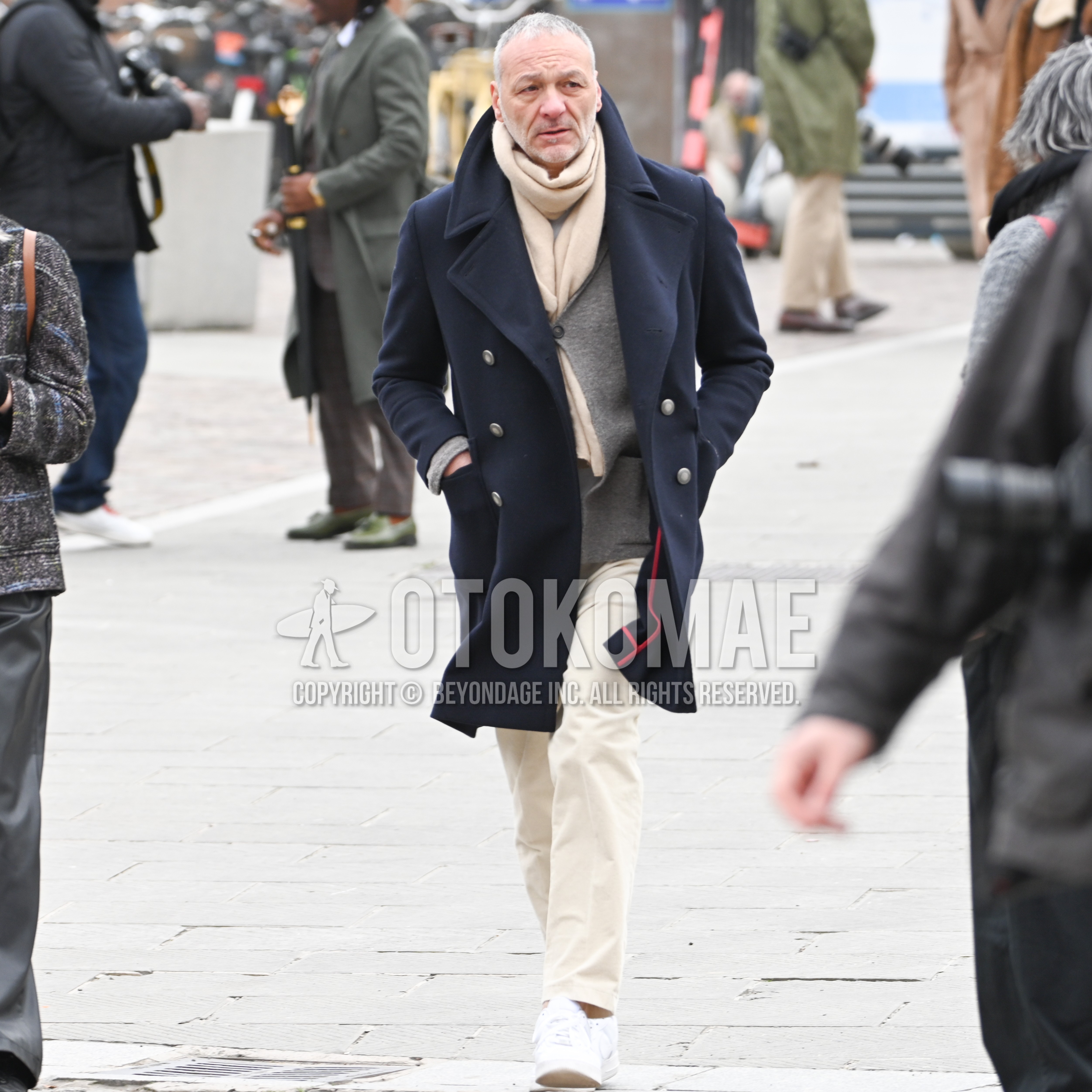 Men's winter outfit with beige plain scarf, navy plain ulster coat, gray plain cardigan, beige plain cotton pants, white low-cut sneakers.