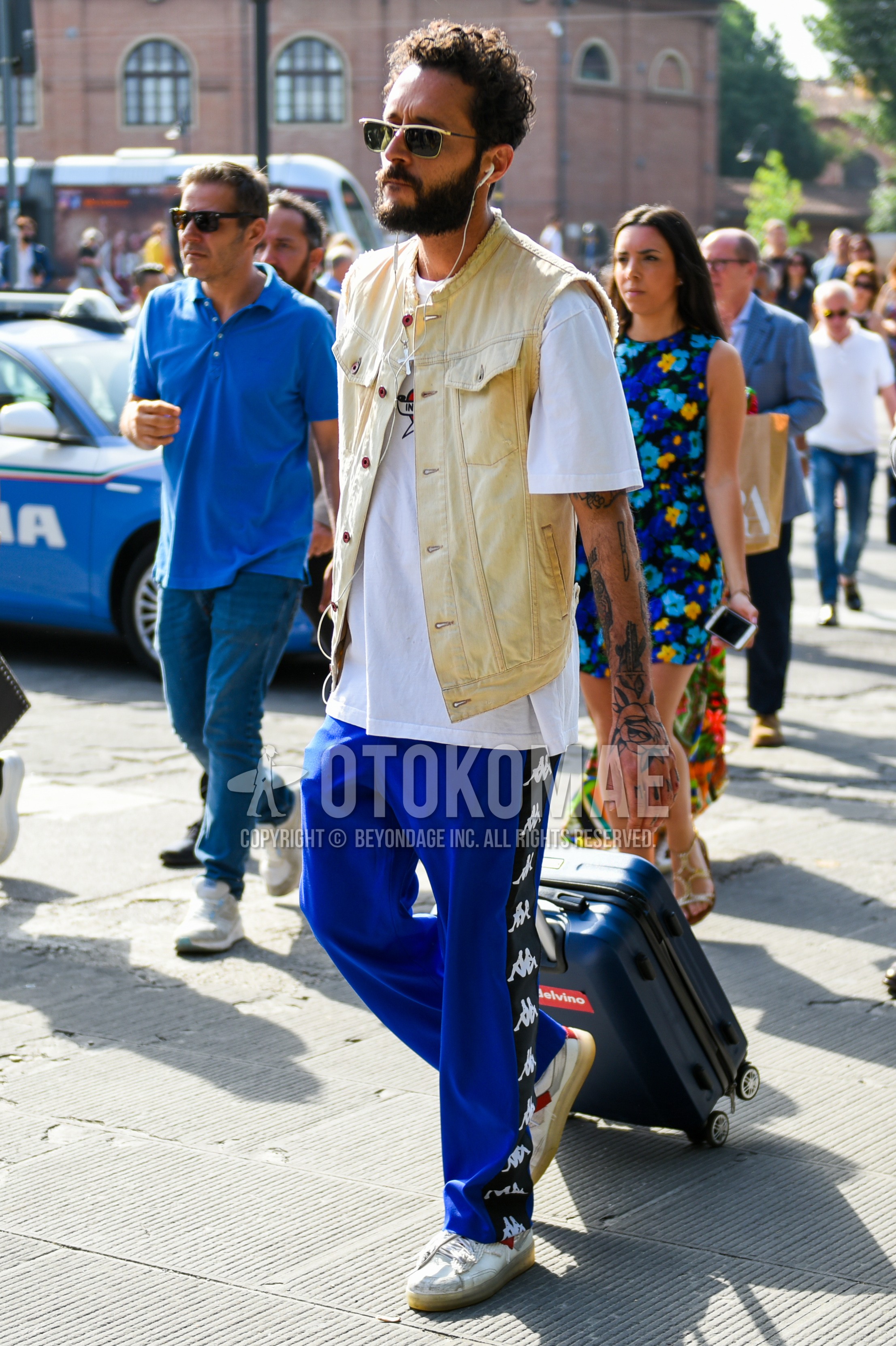 Men's summer outfit with gold plain sunglasses, beige plain denim jacket, white plain t-shirt, blue plain sideline pants, white low-cut sneakers.